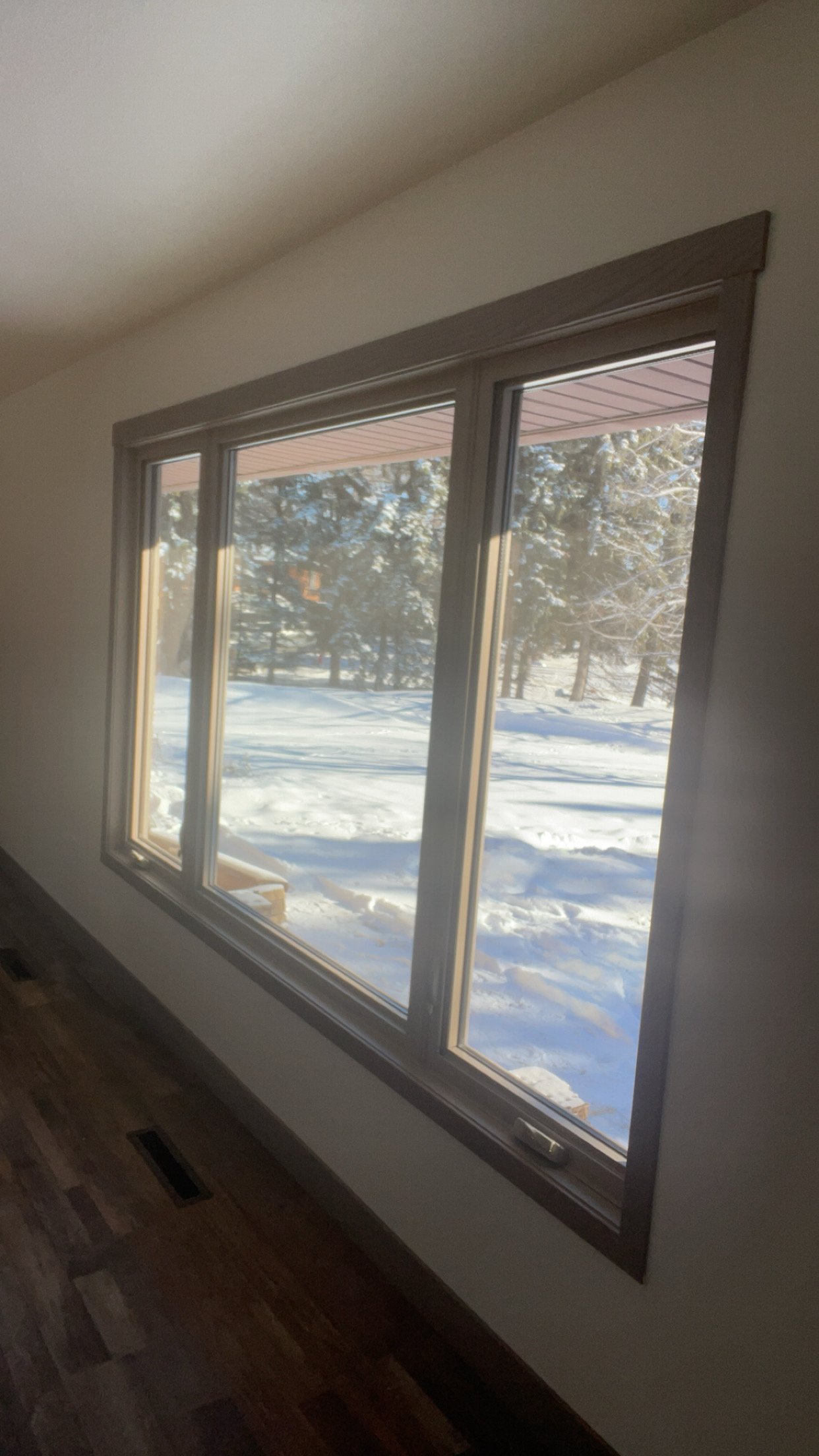 Snow-covered outdoor landscape through a large window in a room with wooden flooring.