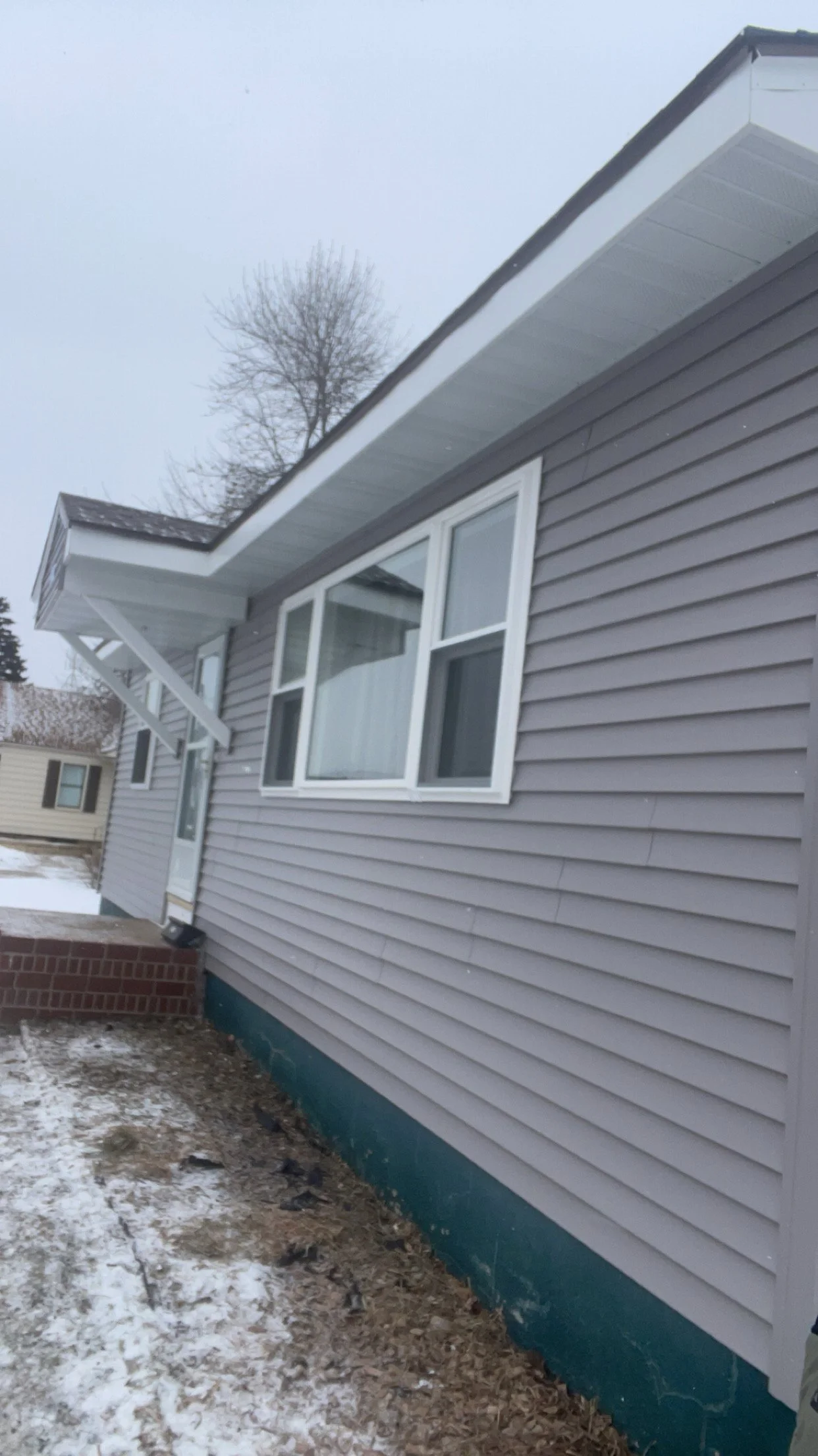 Side view of a house with gray siding, white trim, and a snow-covered yard.