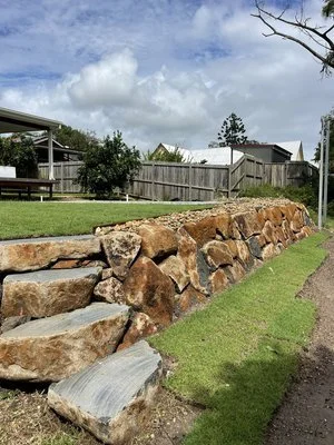 Stone retaining wall with grassy yard and wooden fence in suburban neighborhood.