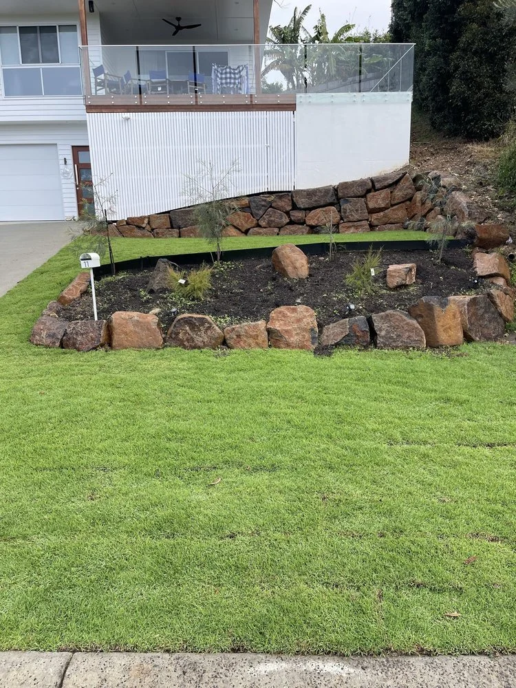 Lawn with landscaping using large rocks and young plants in front of a house with a modern porch.
