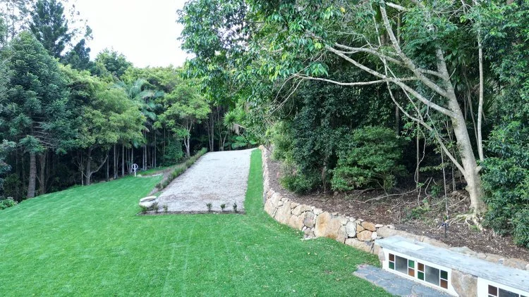 Lush landscape with green grass, a stone wall, and trees alongside a gravel pathway.