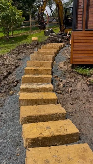 Stone steps under construction in a garden with excavator nearby.