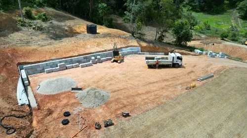 Construction site with retaining wall, gravel piles, excavator, and truck