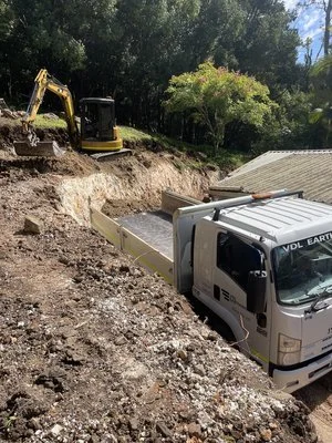 Excavator and dump truck at a construction site with soil and trees.