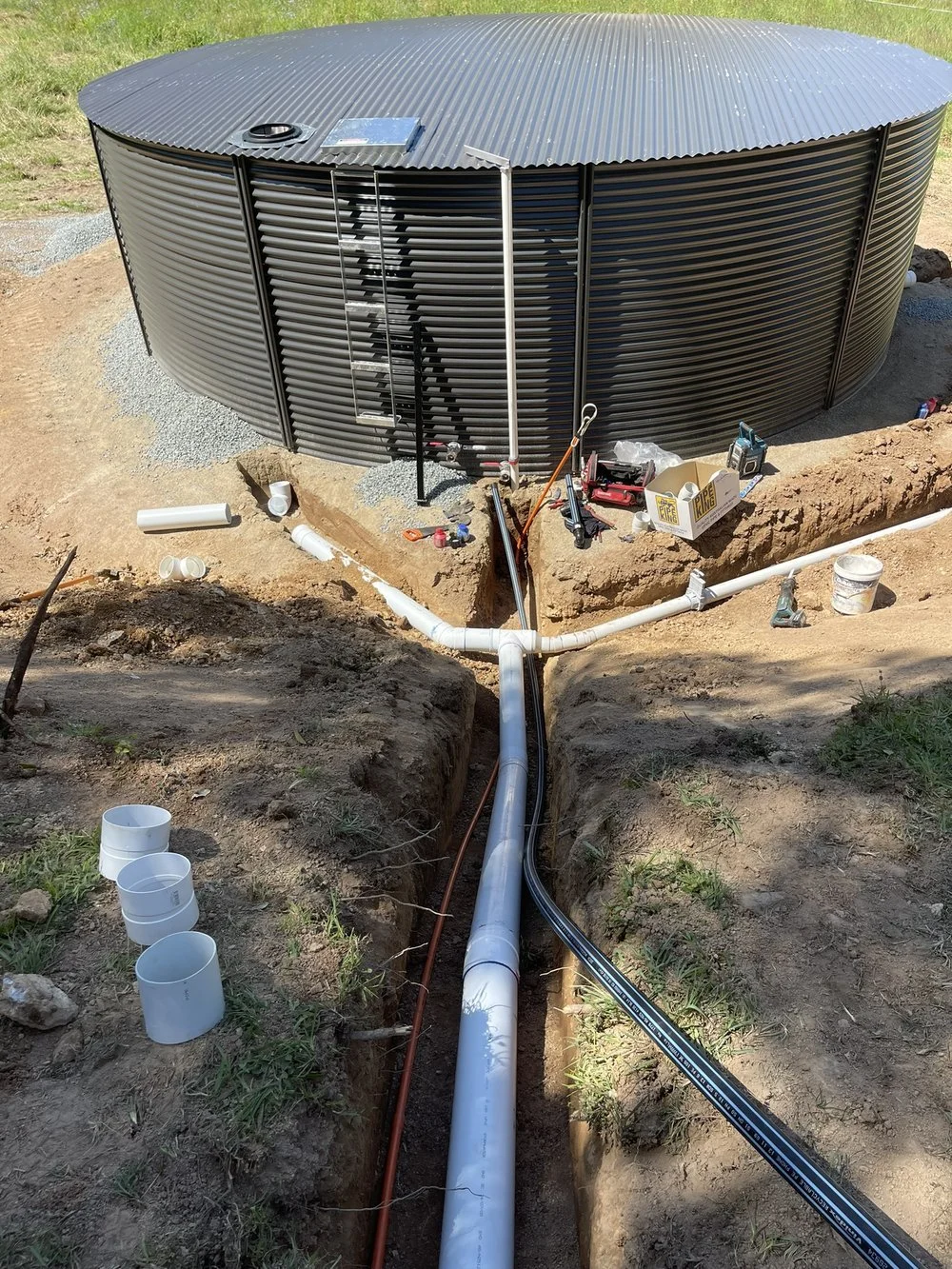 Large metal water tank with surrounding trench and visible piping, tools, and materials.