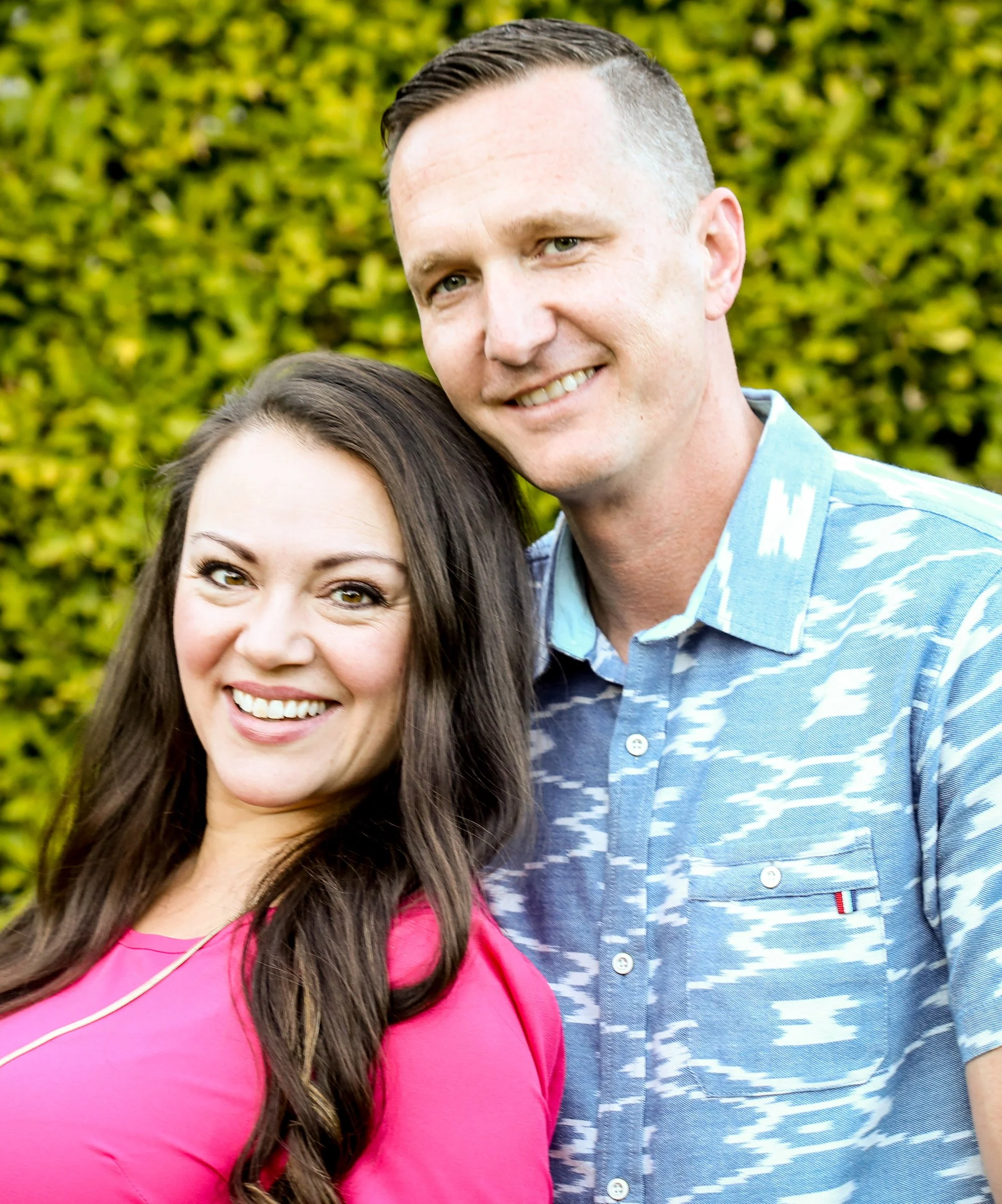 Andrea and Jeff Ballus, standing outdoors with a green bush background.