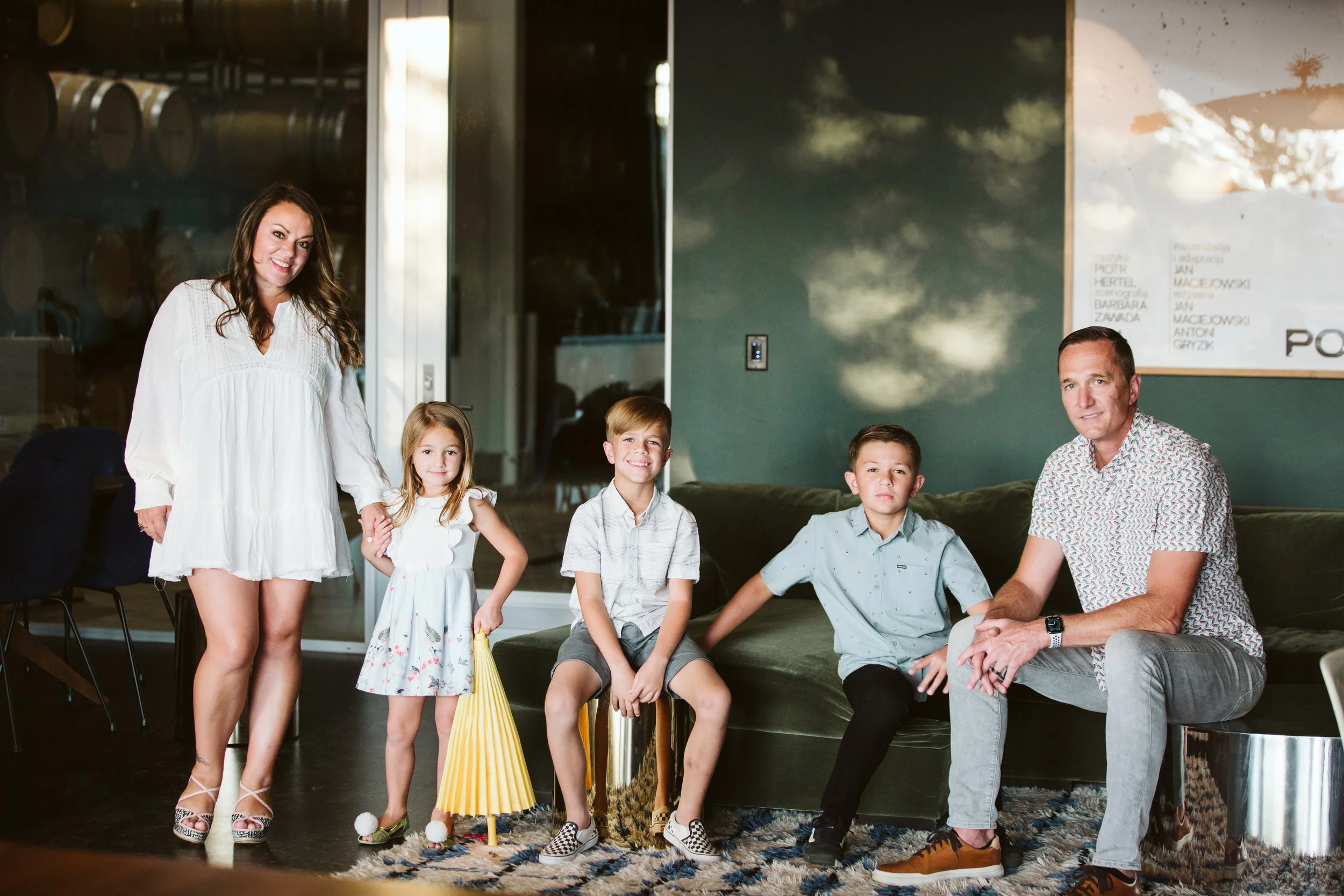 Andrea Ballus and Jeff Ballus with family at Ashes & Diamonds Winery sitting on a dark green couch in a modern living room.