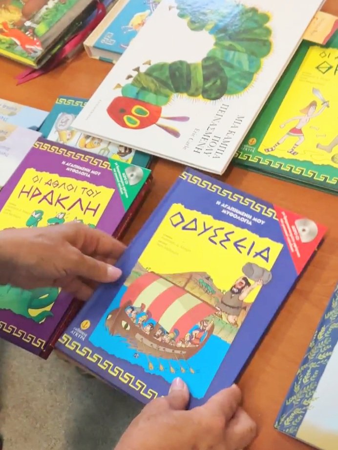 hands holding greek language childrens books on a brown wood table at a school in a rural greek village