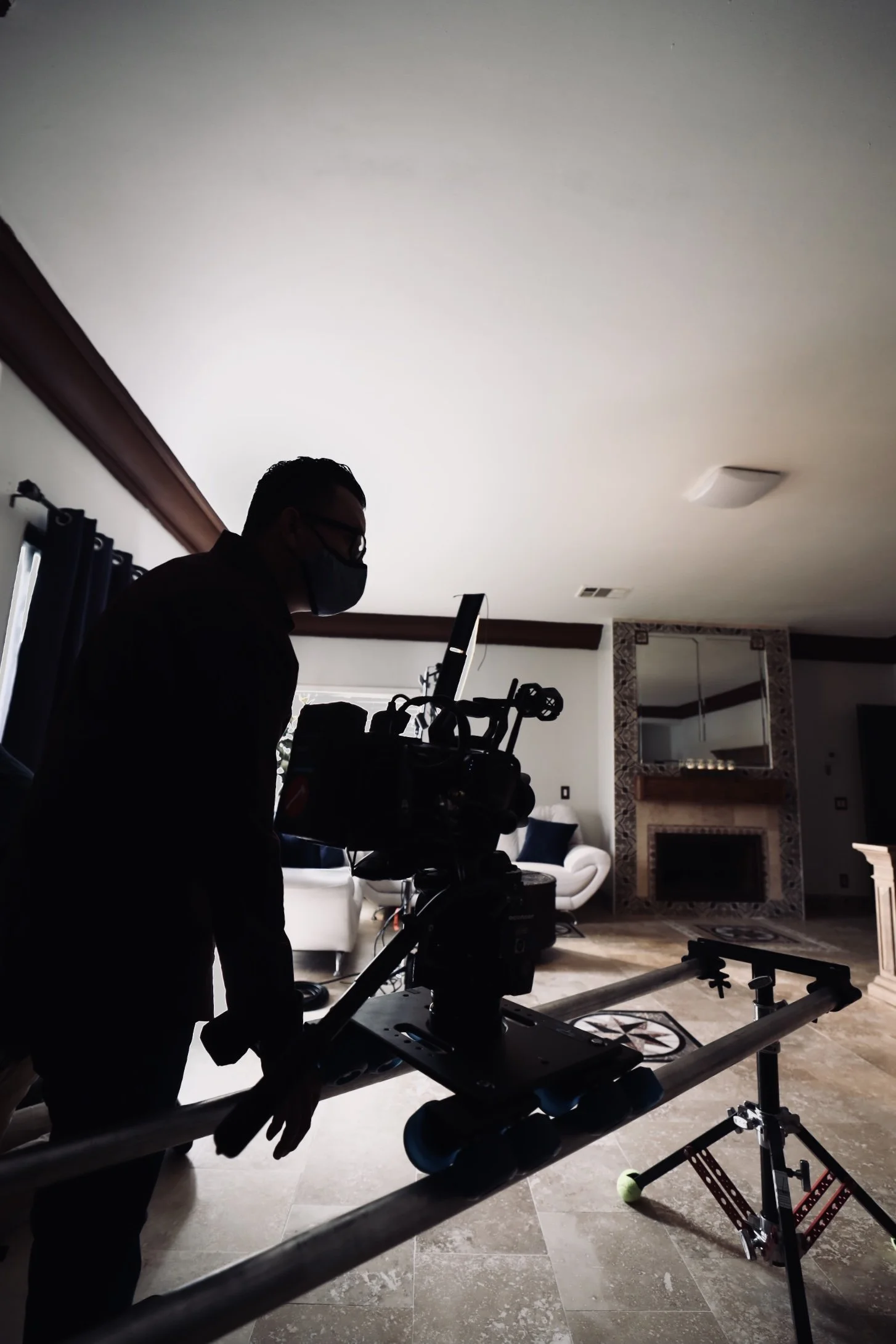 Silhouette of a person operating a professional camera on a dolly track in a living room setting with a fireplace.