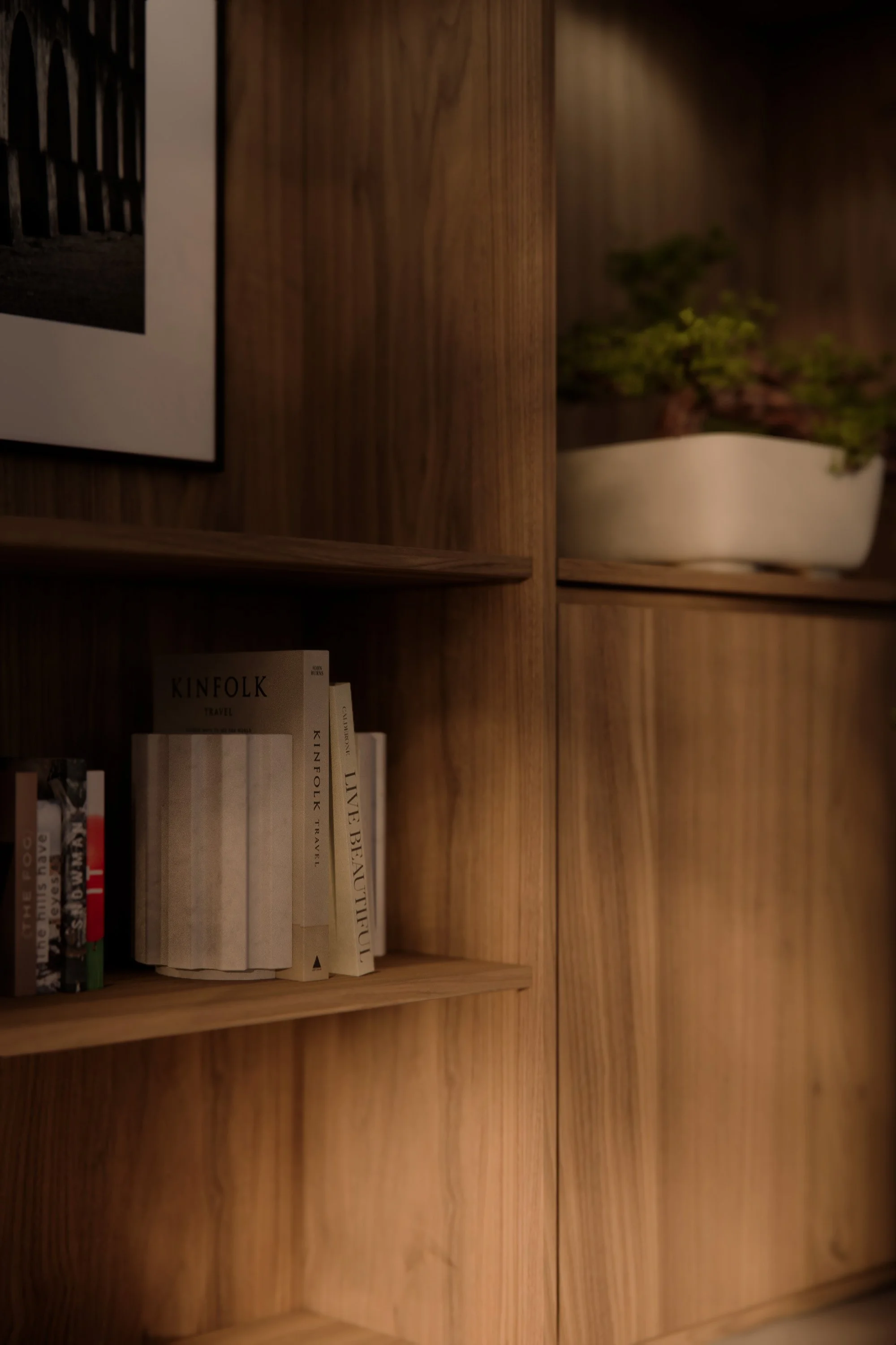 Wooden bookshelf with books, a black-and-white framed photo, and a white ceramic planter with greenery.