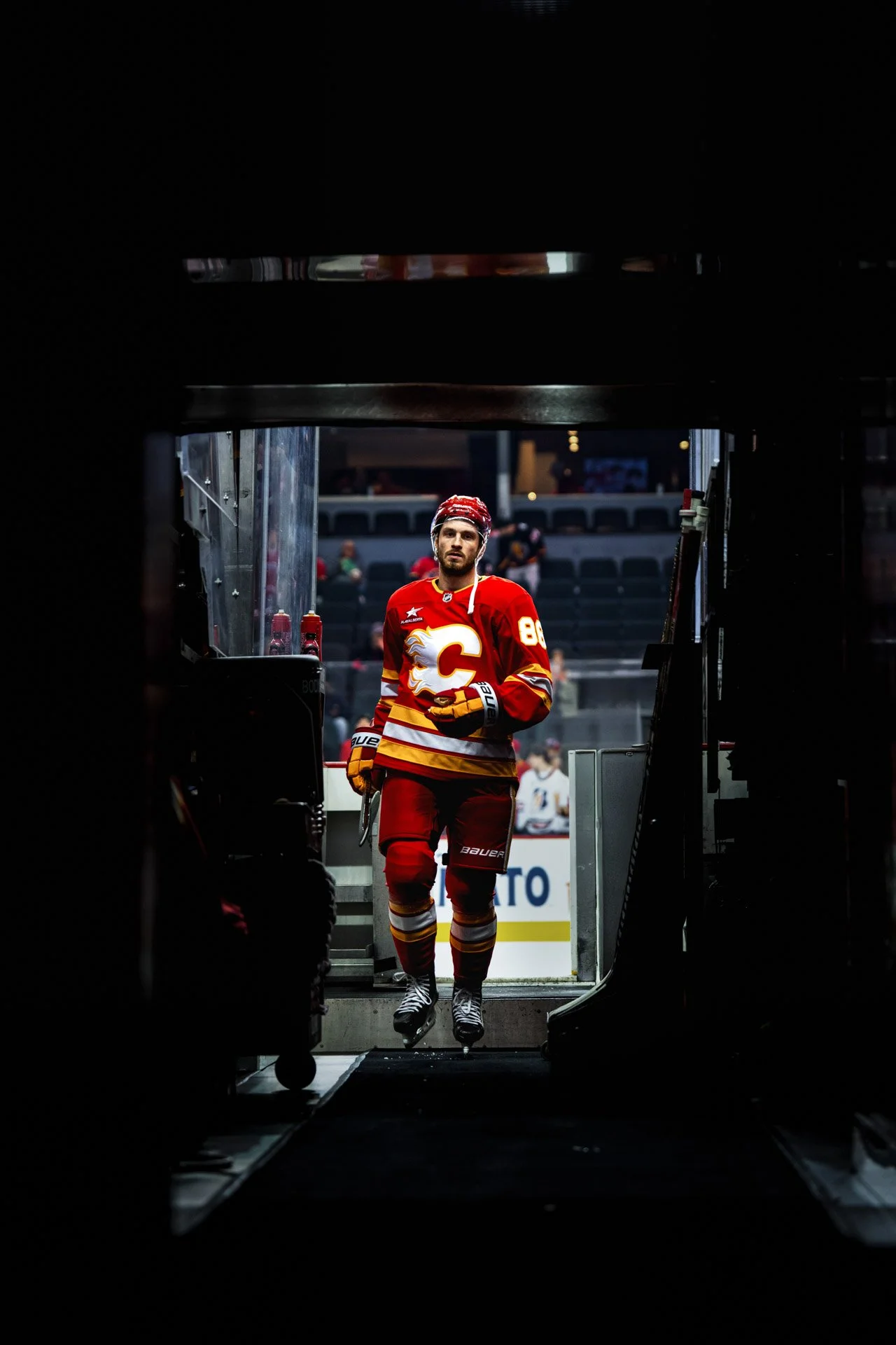 A hockey player in a red Calgary Flames jersey emerging from the tunnel onto the ice rink.