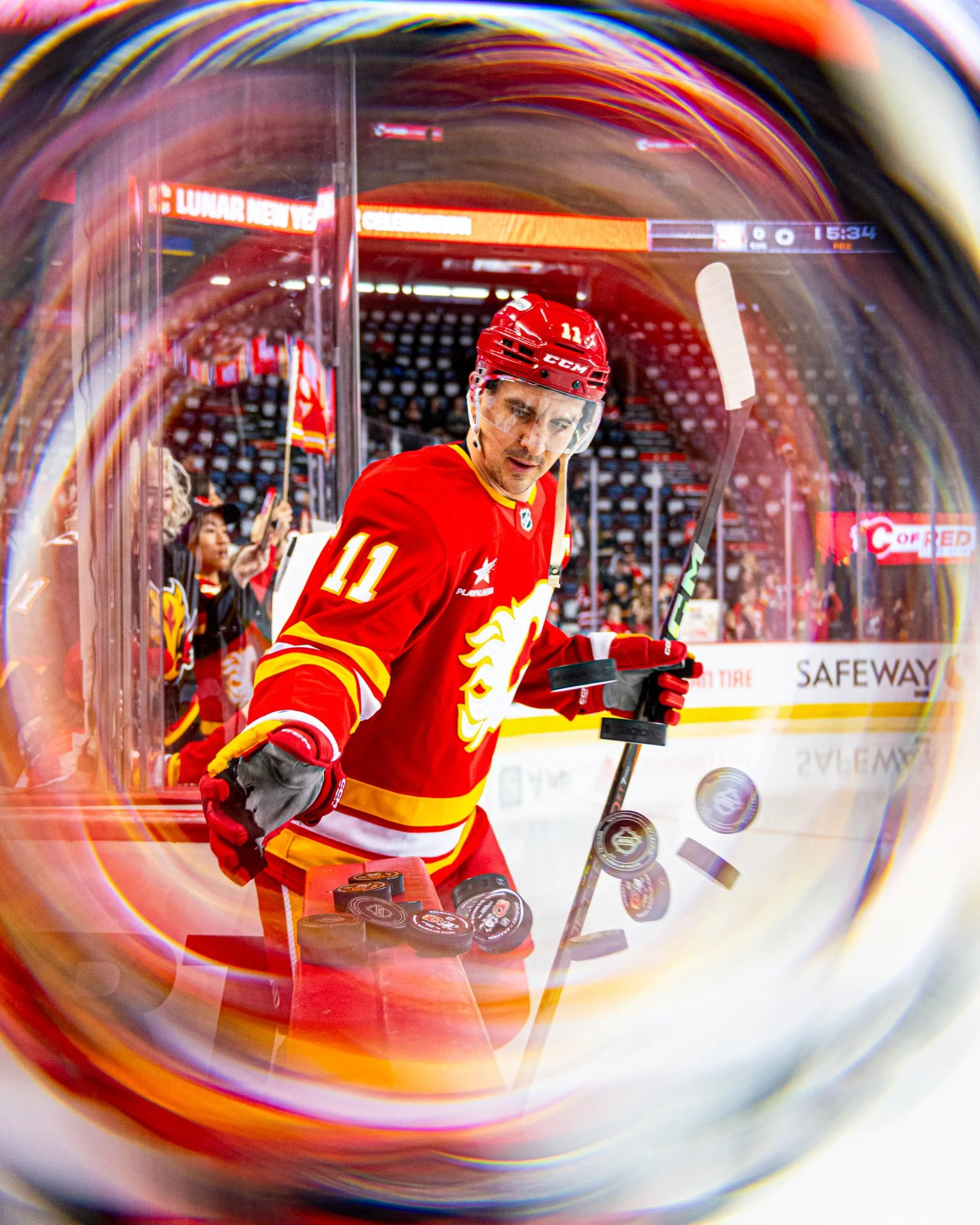 Hockey player in red uniform number 11, hockey stick in hand, on the ice rink during a game.