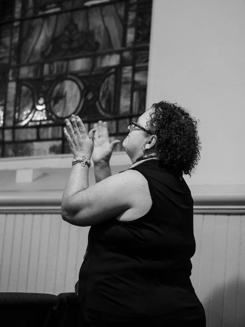 A woman clapping in front of a stained glass window.