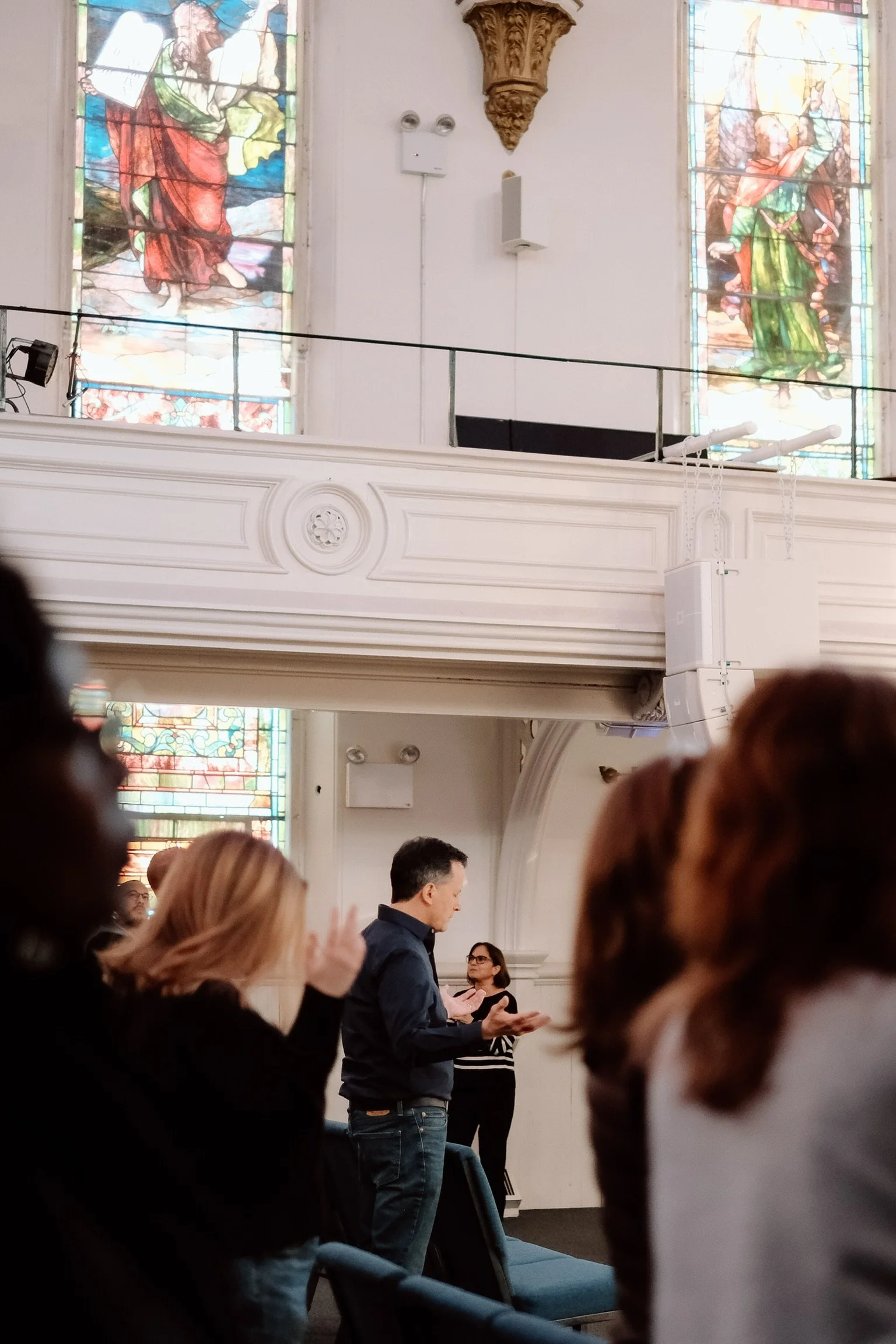 People standing and singing in a church with stained glass windows in the background.