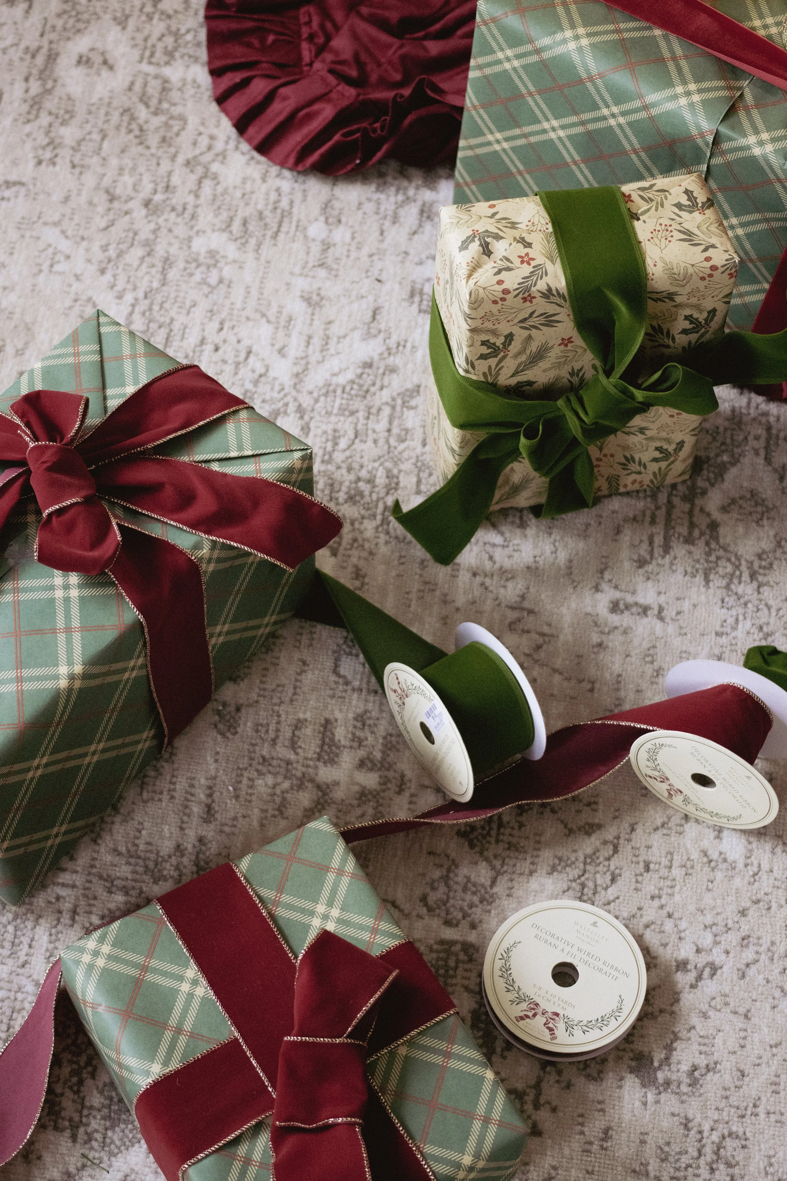 Various wrapped Christmas presents with ribbons and bows on a carpeted floor.