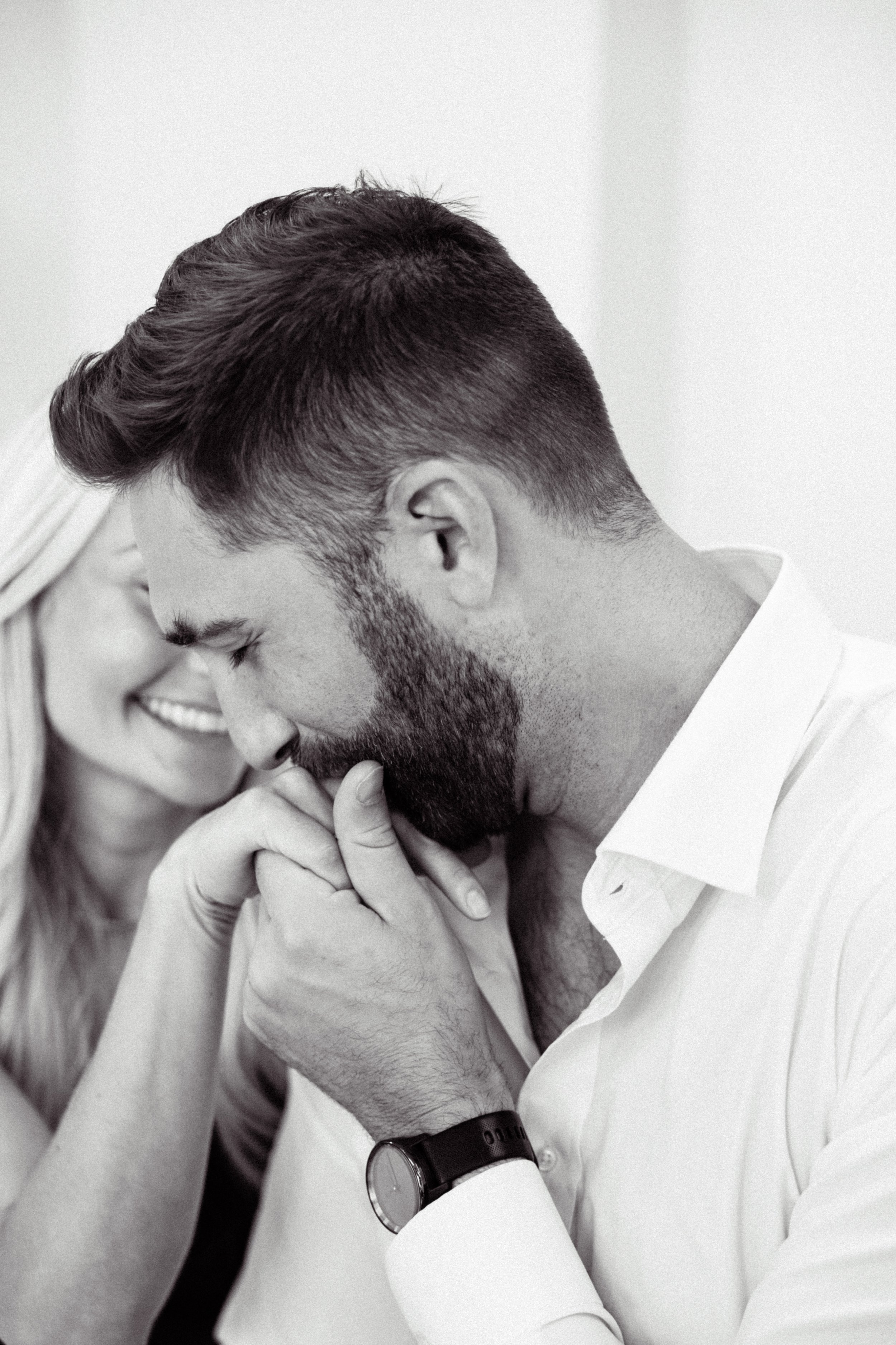 A black-and-white photo of a man with a beard and a woman smiling, holding hands close to each other's faces.