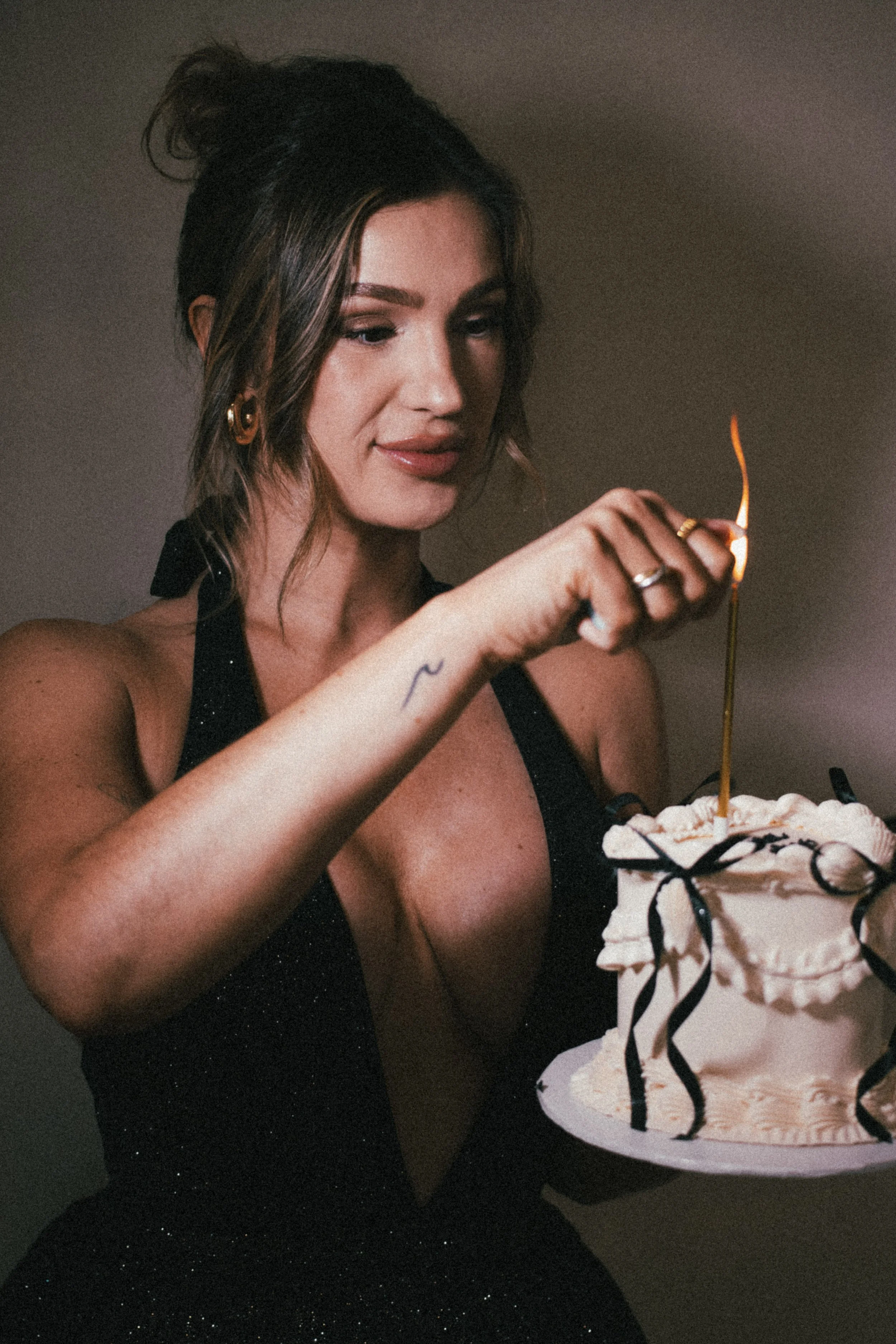 A woman with dark hair and makeup holding a cake with a lit candle.