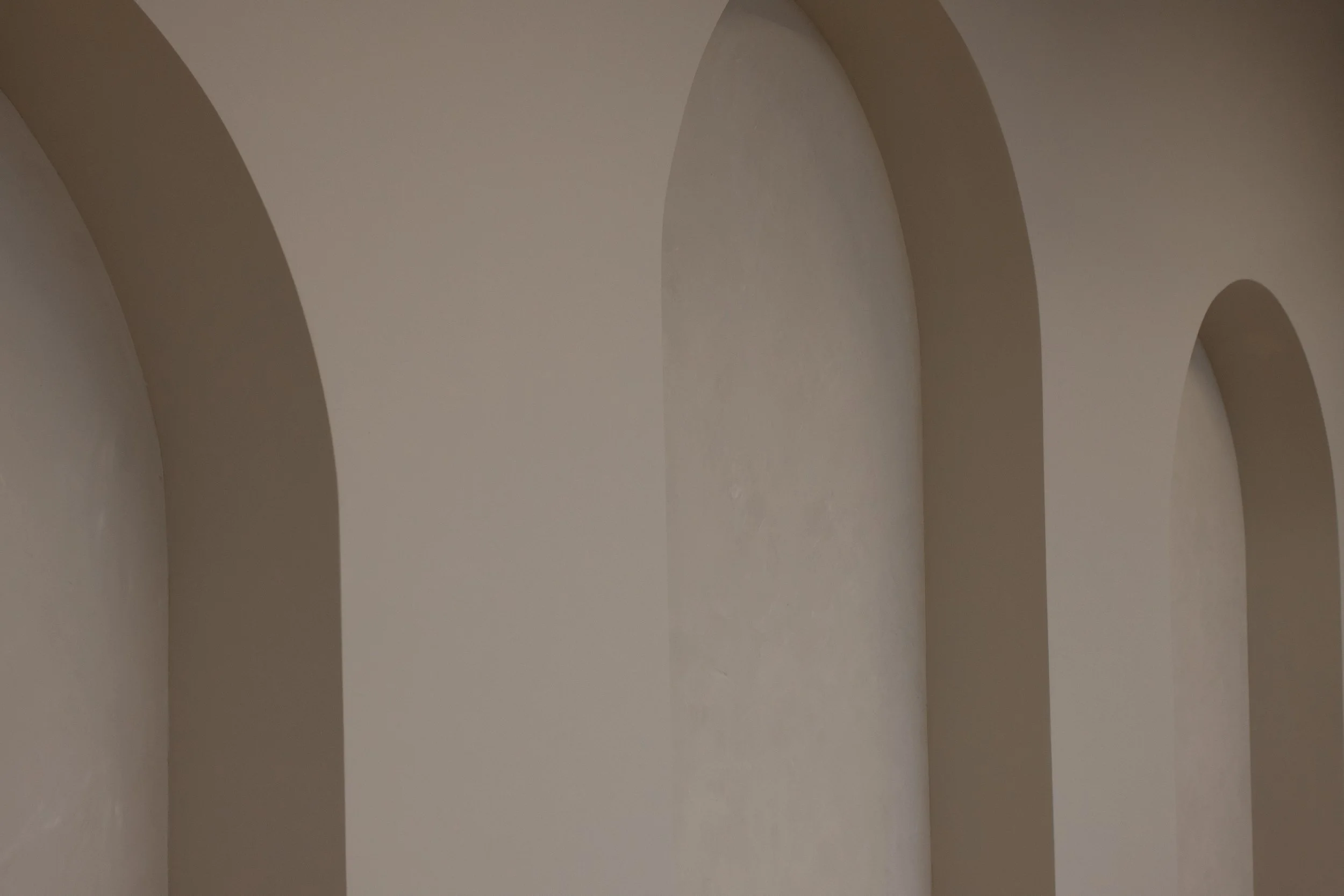 A series of large, beige, rounded arches in a soft, neutral-colored wall.