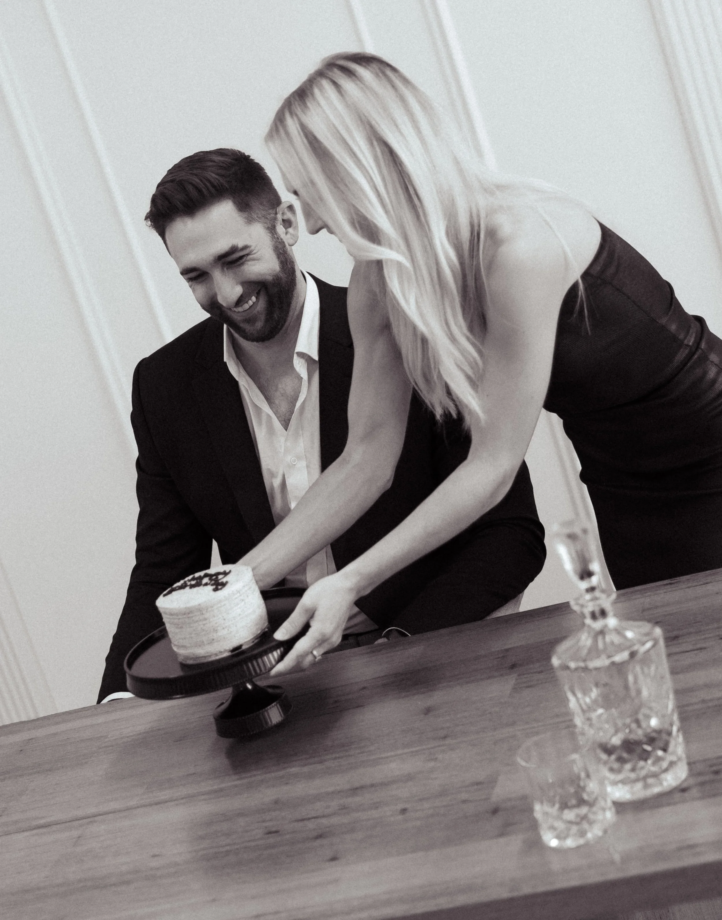 A man and woman cutting a cake at a celebration, with the woman placing the cake on a plate. The scene is in black and white.