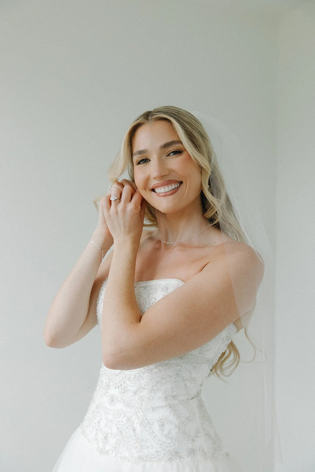 White wedding dress hanging on a decorative gold hanger on a white wall.