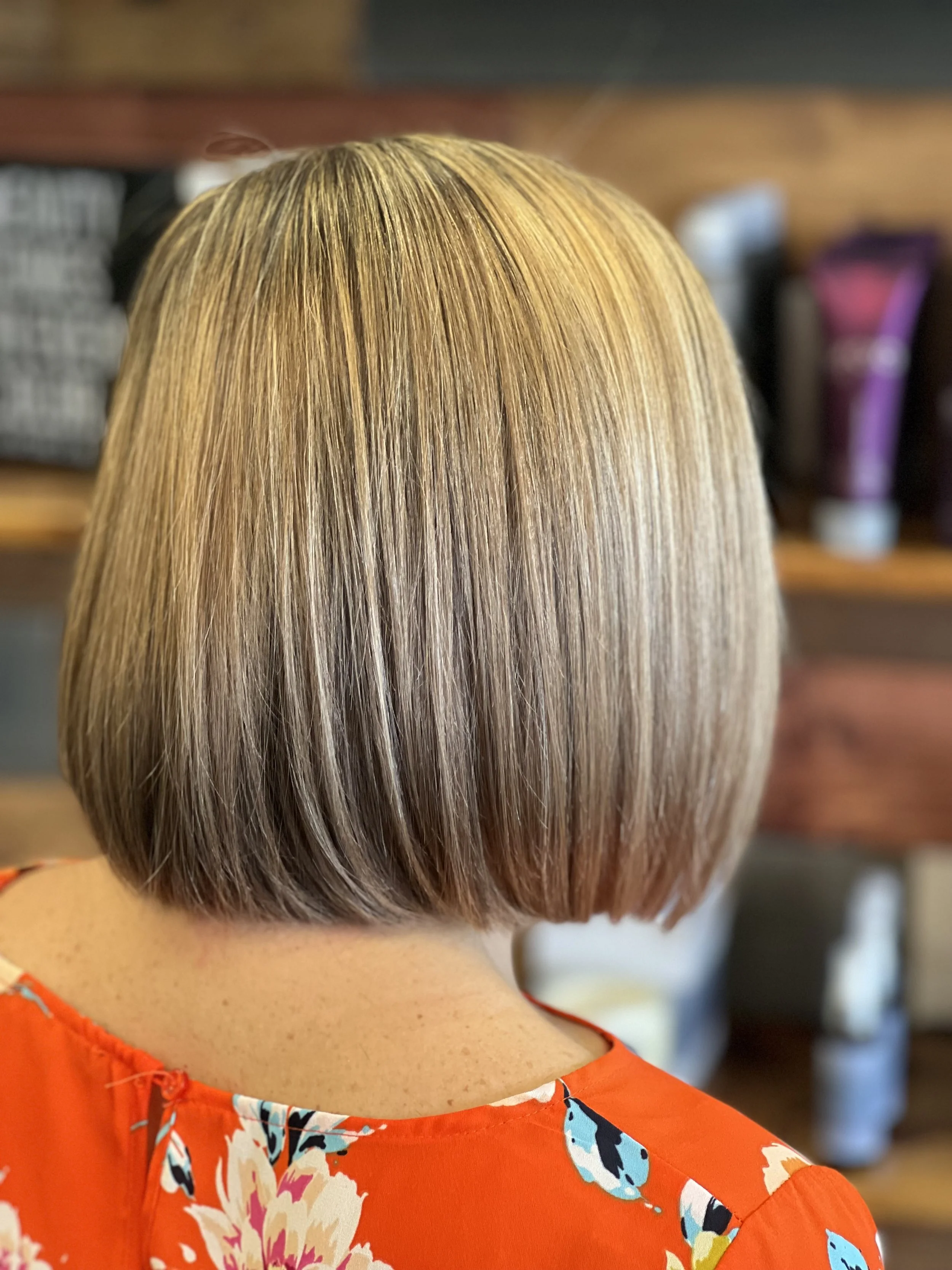 Back of a person's head with straight, shoulder-length blonde hair and an orange floral top.