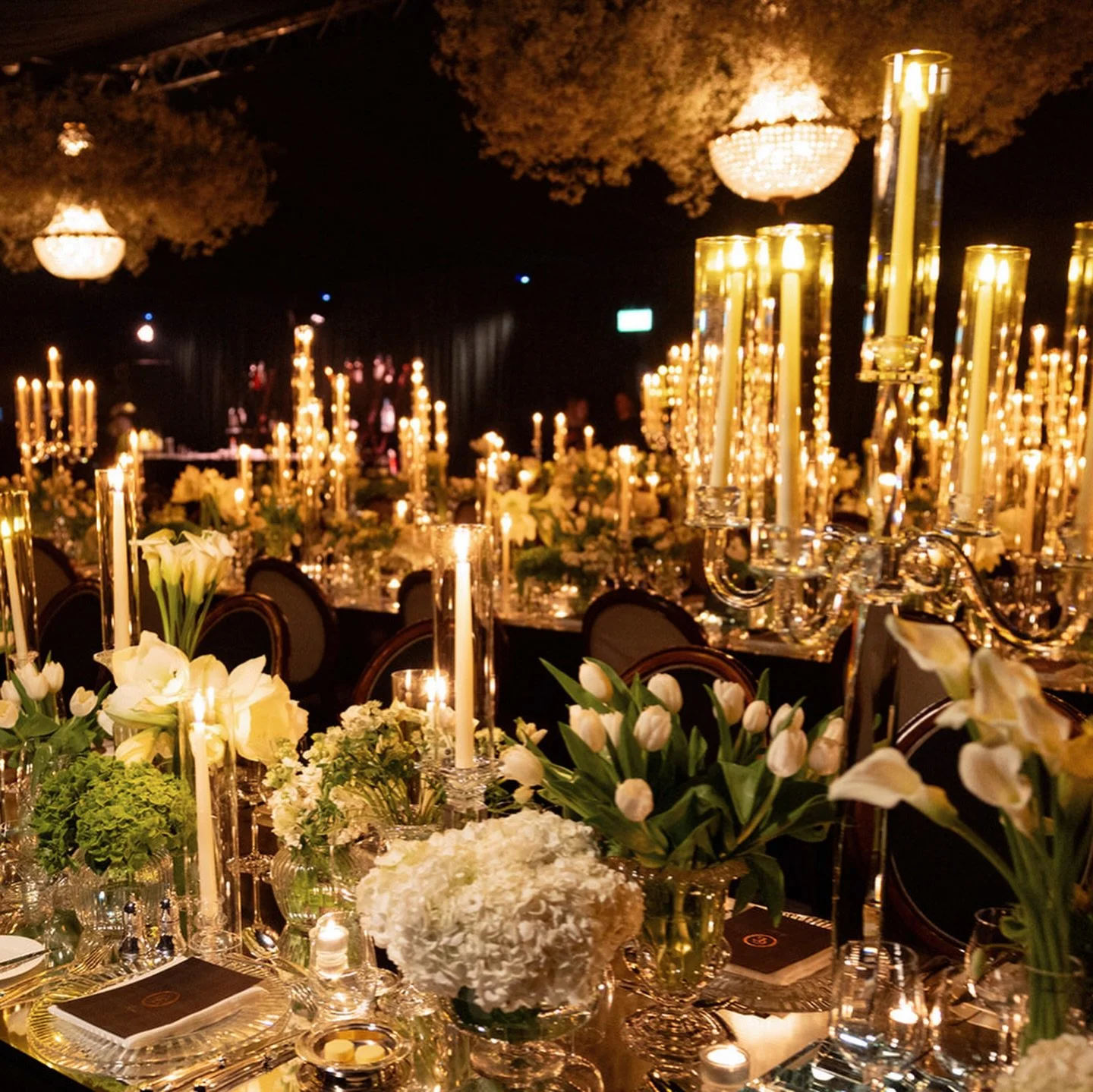 The room was fully draped in rich dark green velvet, with crystal chandeliers hanging overhead, casting the warmest glow across every table. 
Layers of flowers, flickering flames, and golden reflections turned the night into pure magic ✨ 

Photograph