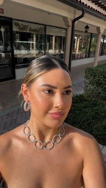 A large ring on the hand. A stud and a small hoop in the ear. A thin necklace with a small pendant.