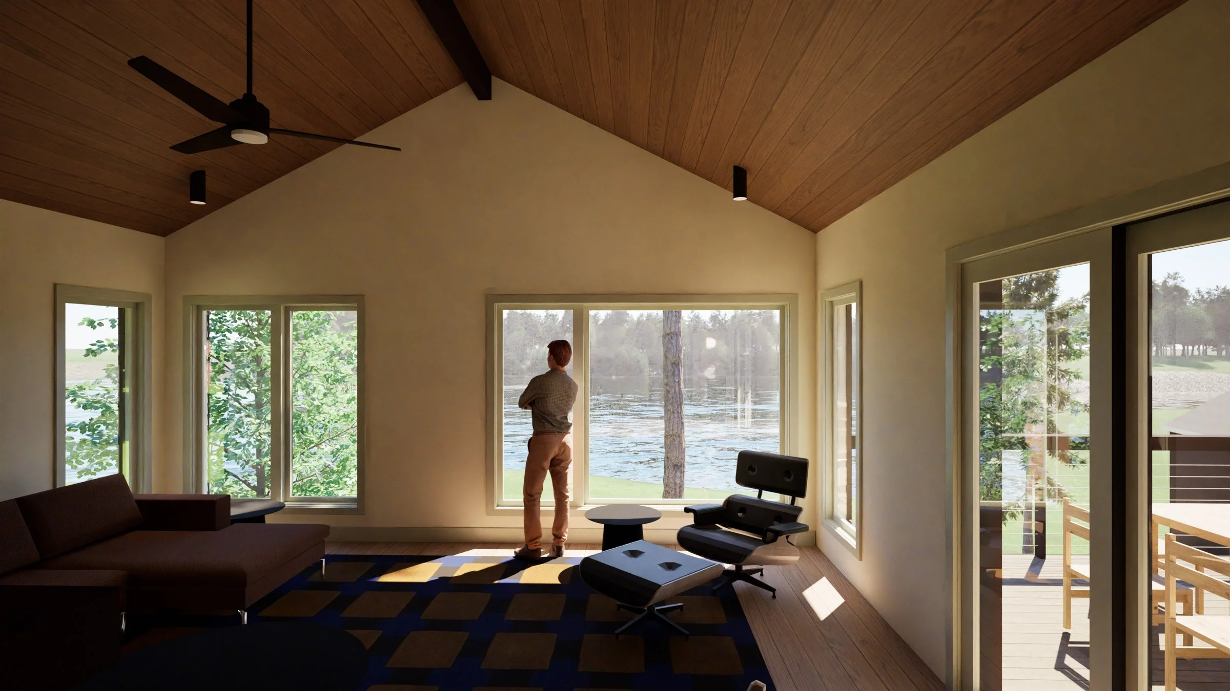 Inside view of a modern home with large windows overlooking a lake and trees, featuring a wooden vaulted ceiling, ceiling fan, black chairs, sofa, and a person looking outside in a new construction cabin / lake house in the Brainerd Lakes Area, MN.
