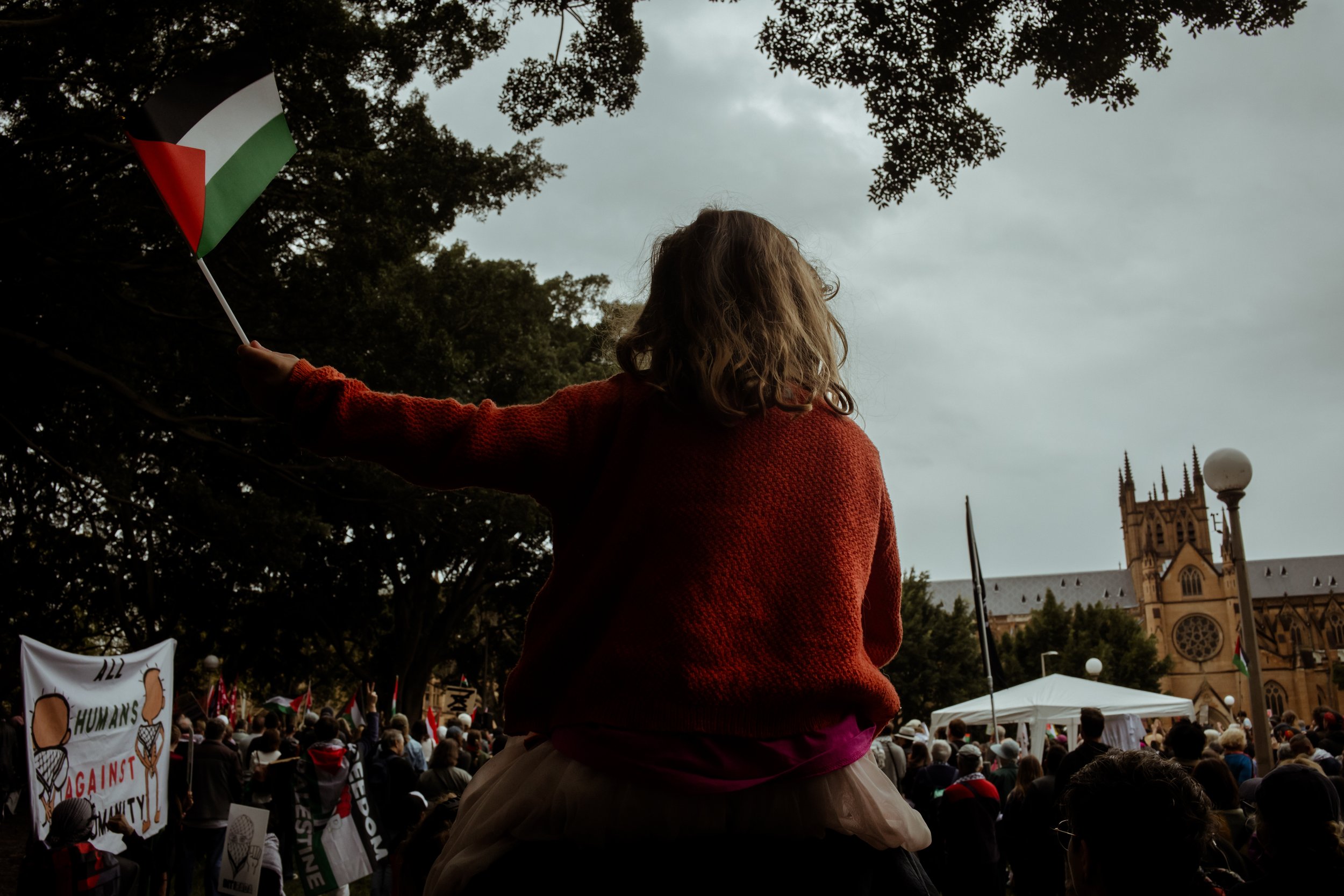 A child on someone's shoulders waving a flag, seen from behind, with St Mary's Cathedral beyond