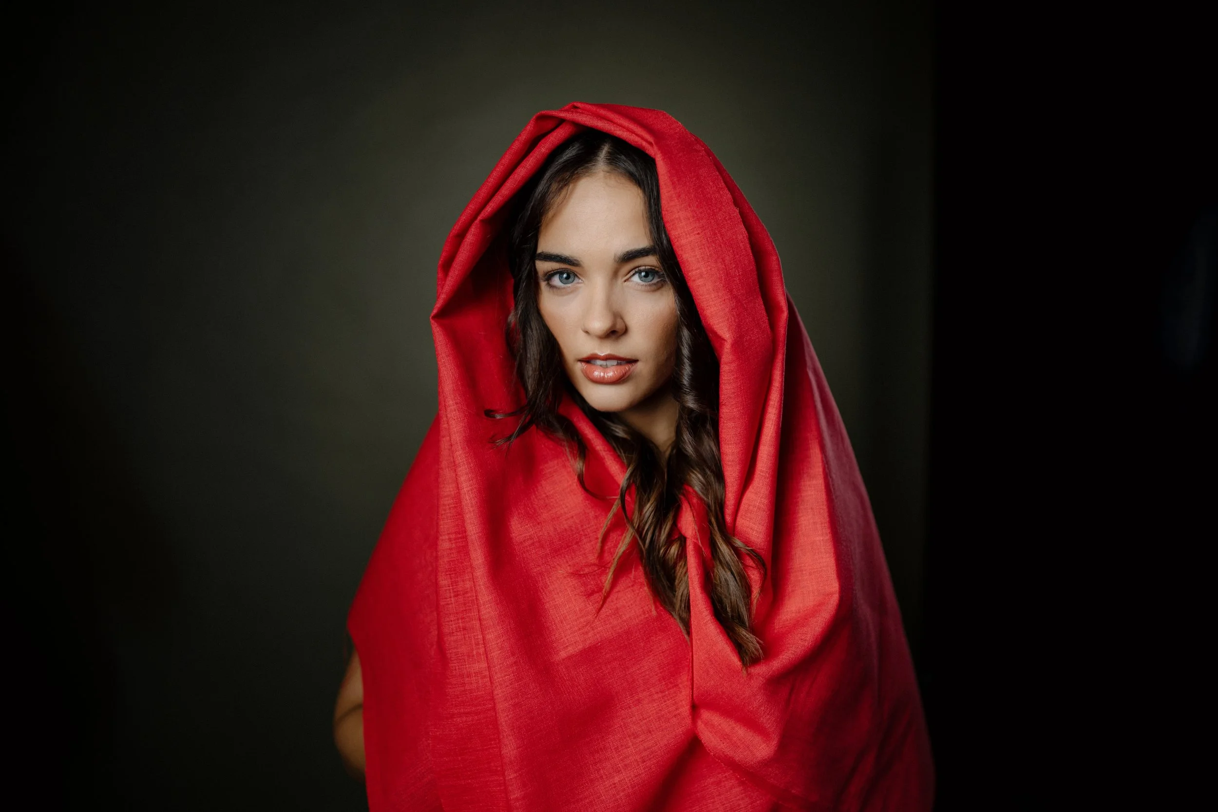 Erin Hobden in a red hood against a dark studio background