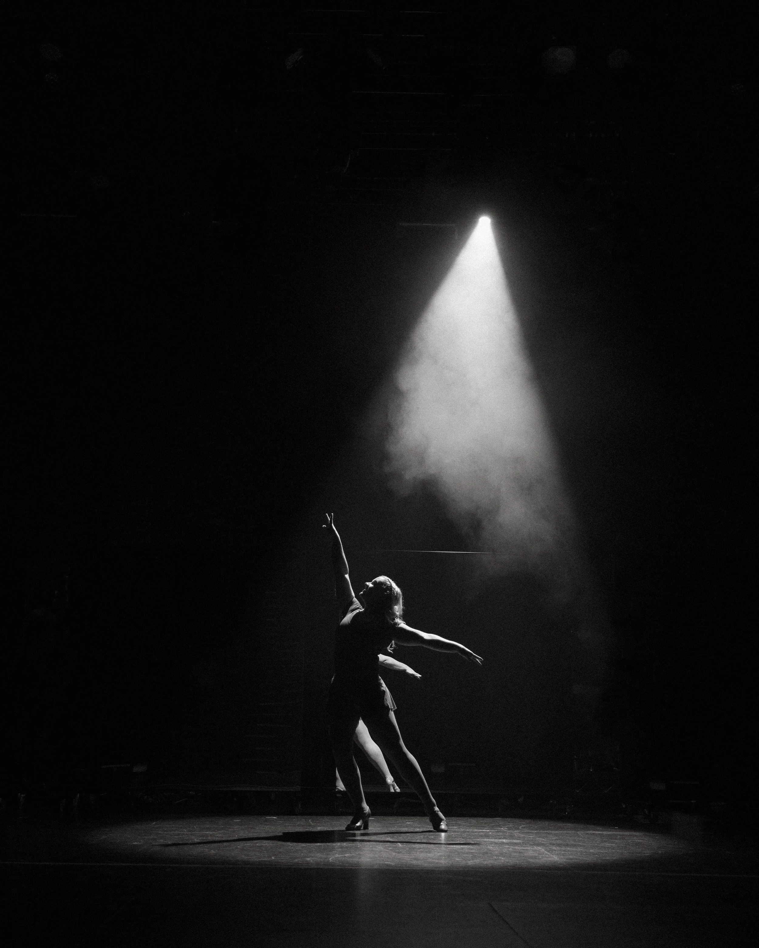 A dancer alone in a cone of light and haze on a dark stage