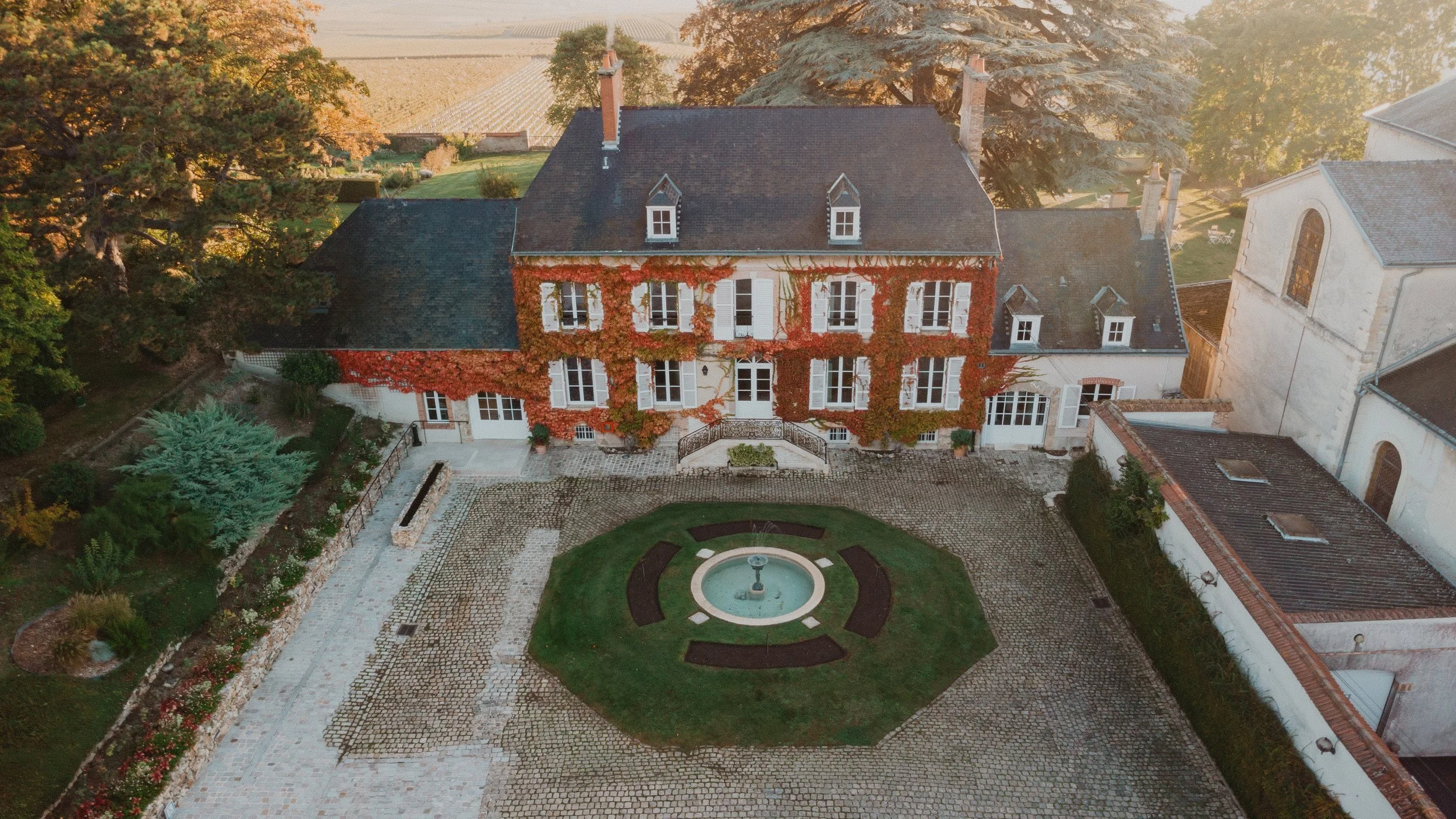 Manoir de Verzy, its circular lawn and fountain from above in early light.