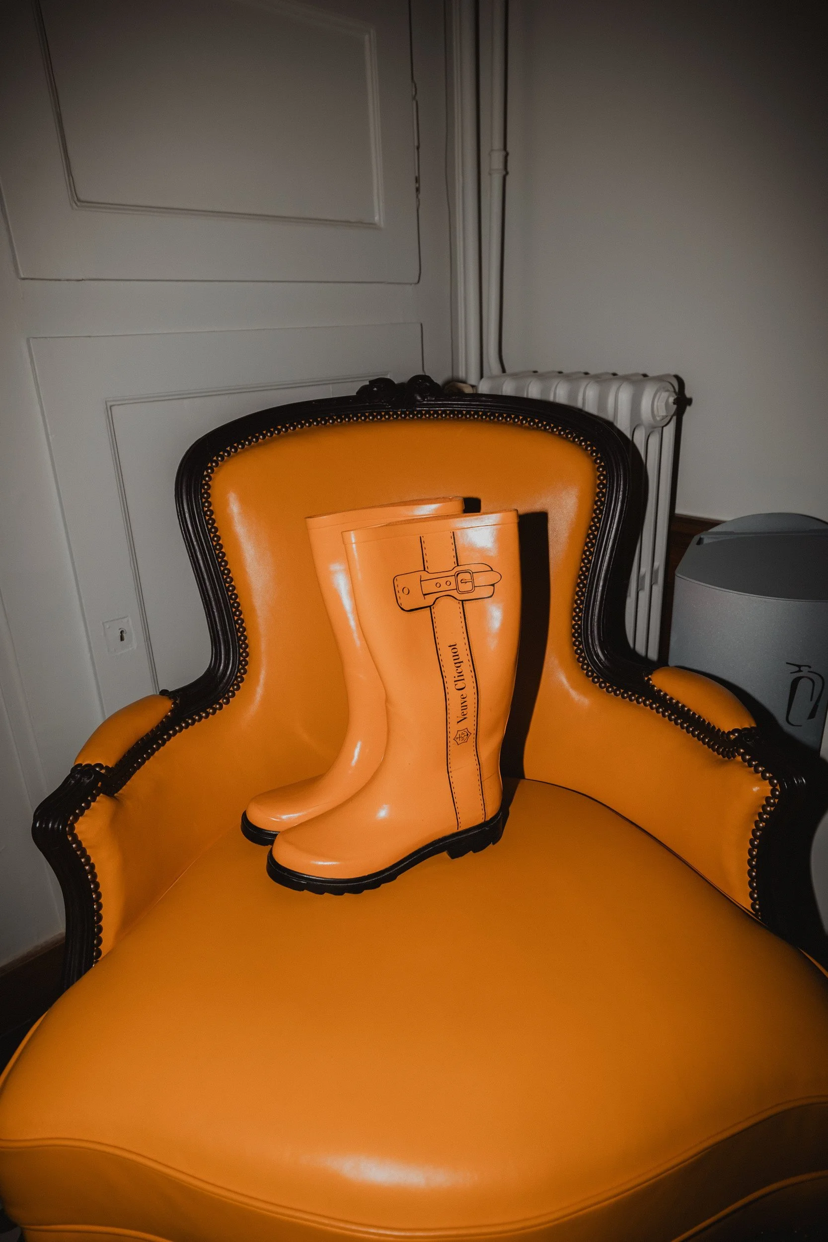Orange wellington boots set on an orange armchair in a pale panelled room.