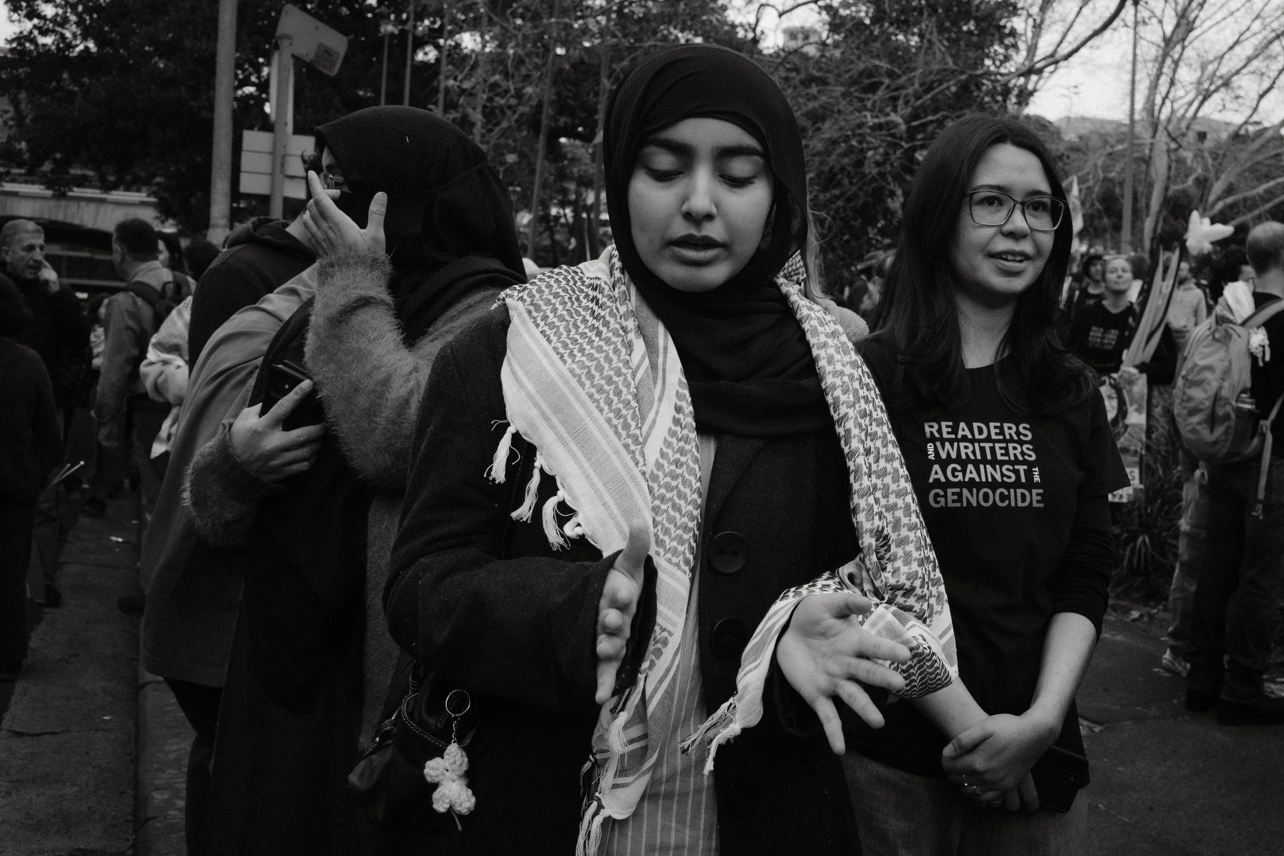 Black and white frame of young women in keffiyehs, gesturing as they talk