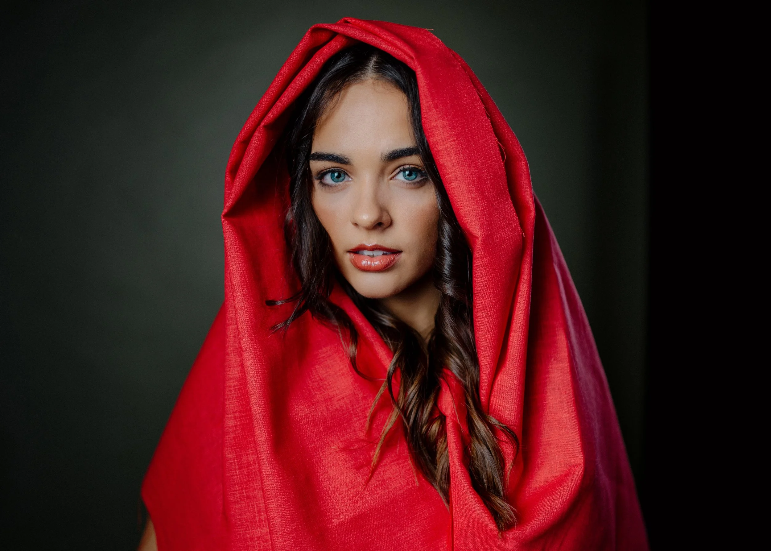 Portrait of Erin Hobden wrapped in a red cloth hood, lit from one side