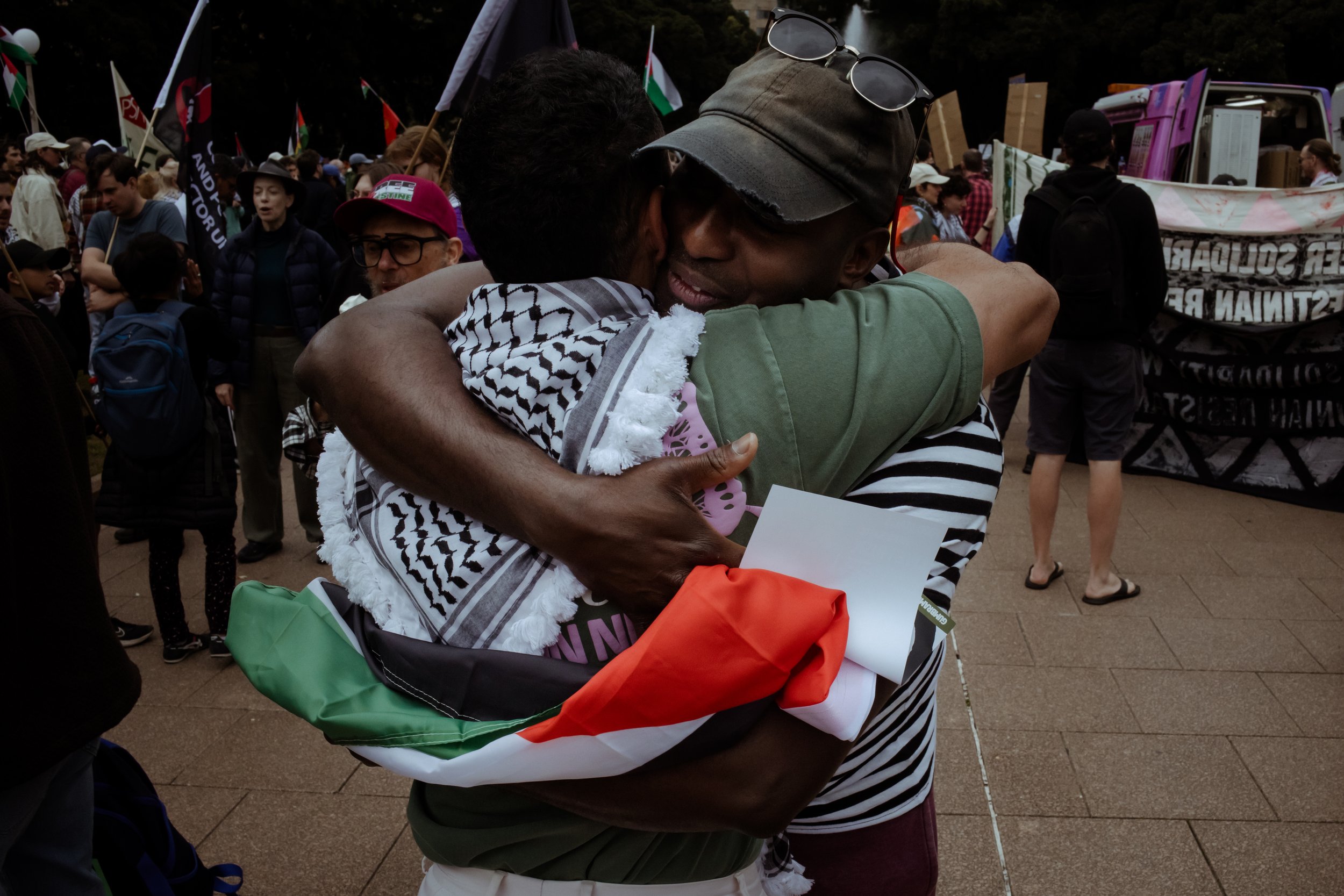 Two marchers embracing beside a flag at the Hyde Park march, Sydney