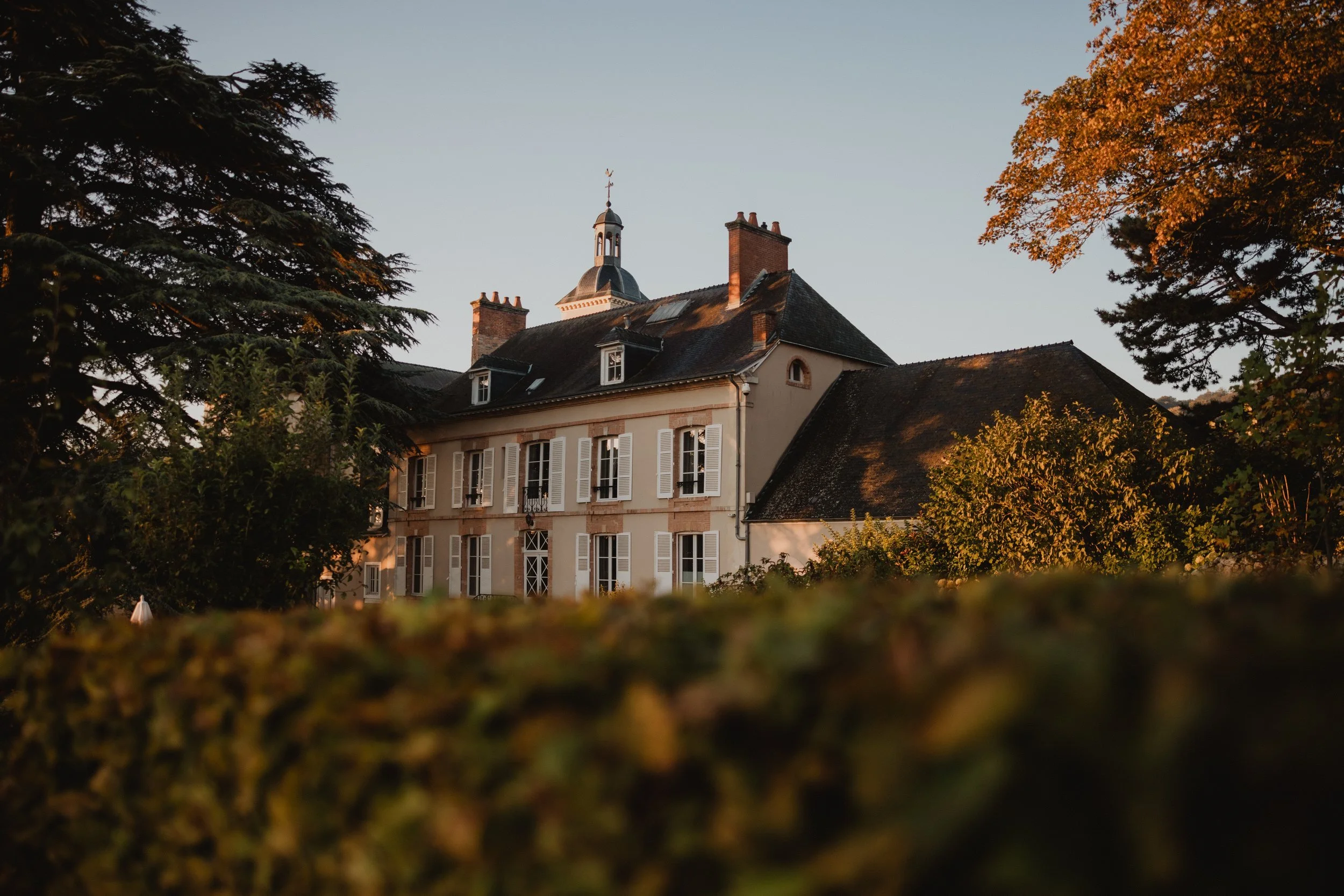 Manoir de Verzy seen low through a clipped hedge, an autumn tree at right.