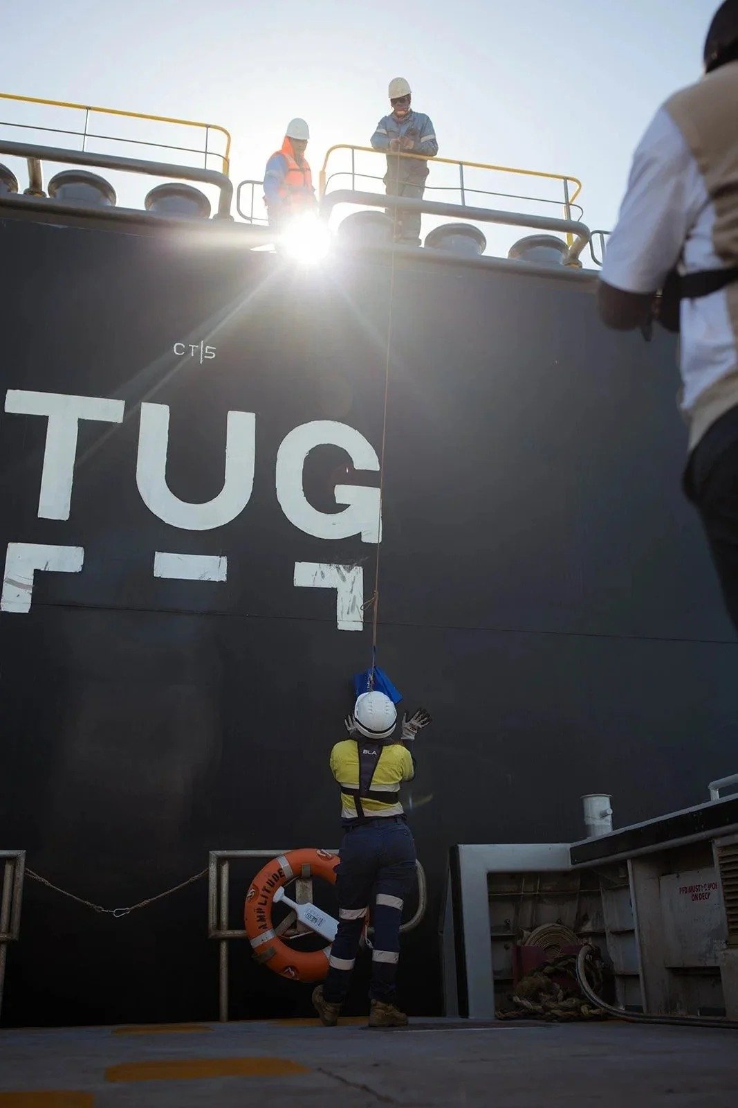 A worker climbs the pilot ladder up the black hull of a tug in Port Hedland harbour