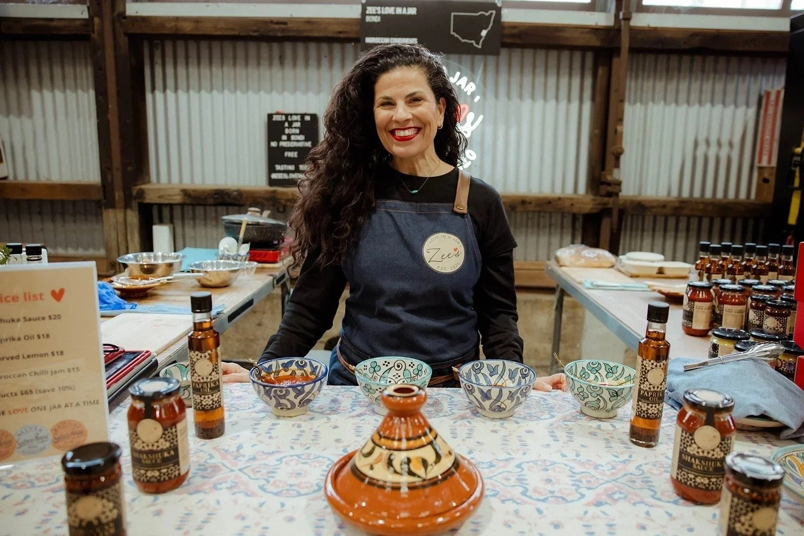 A stallholder smiling behind her table of food at the Carriageworks Winter Seasonal Market