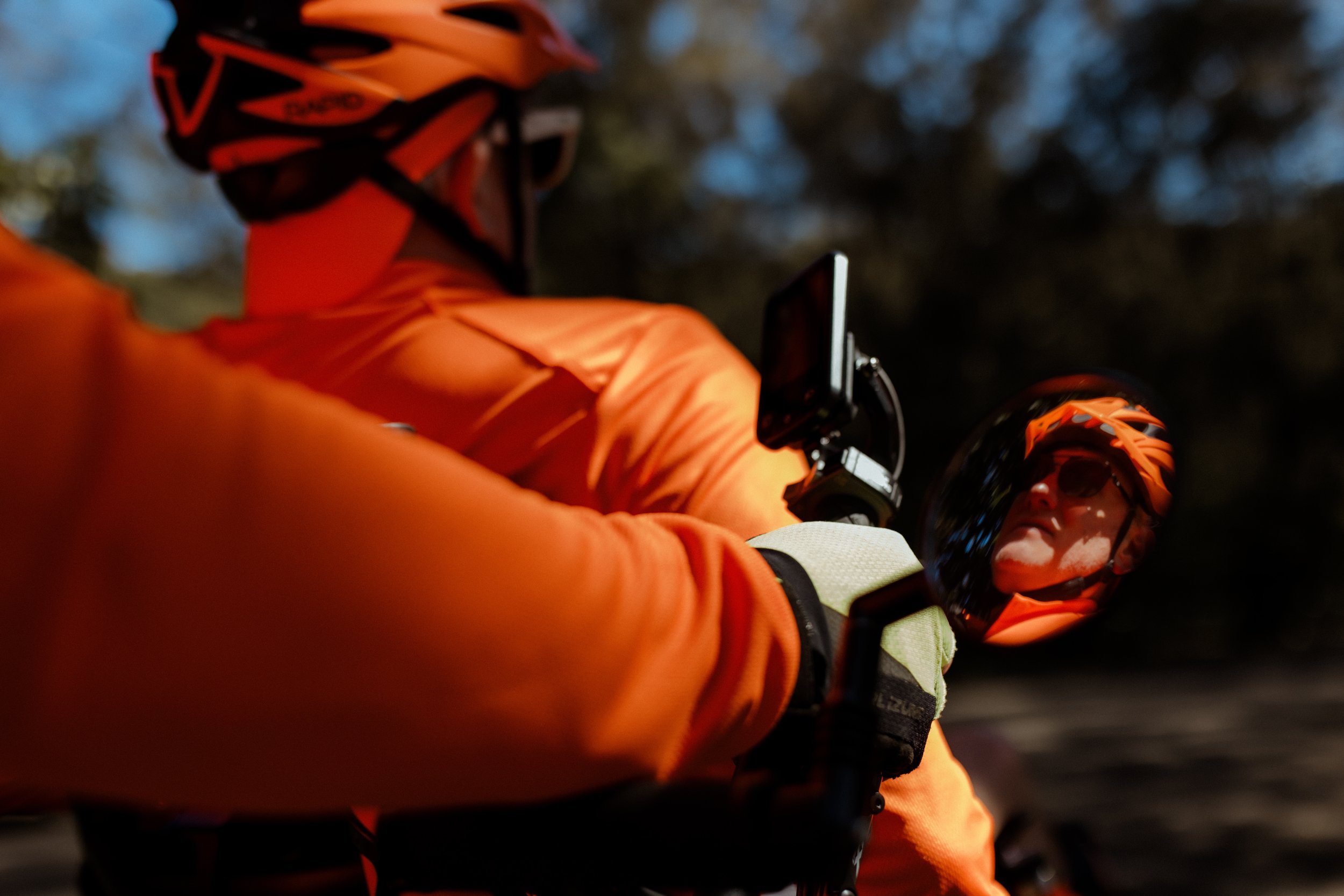 Close detail of a rider in orange reflected in the handlebar mirror