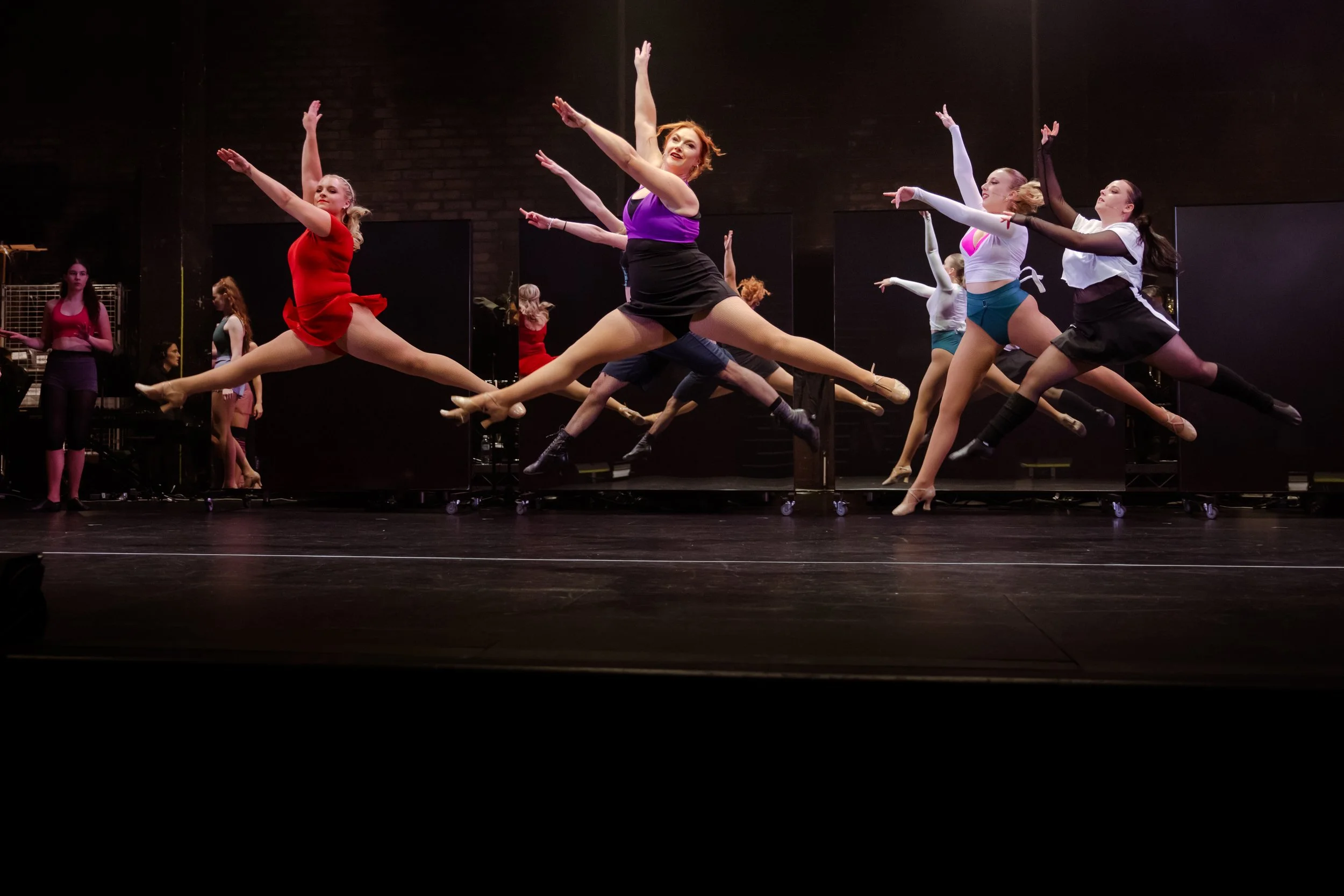 Dancers mid-leap across the stage in rehearsal for A Chorus Line