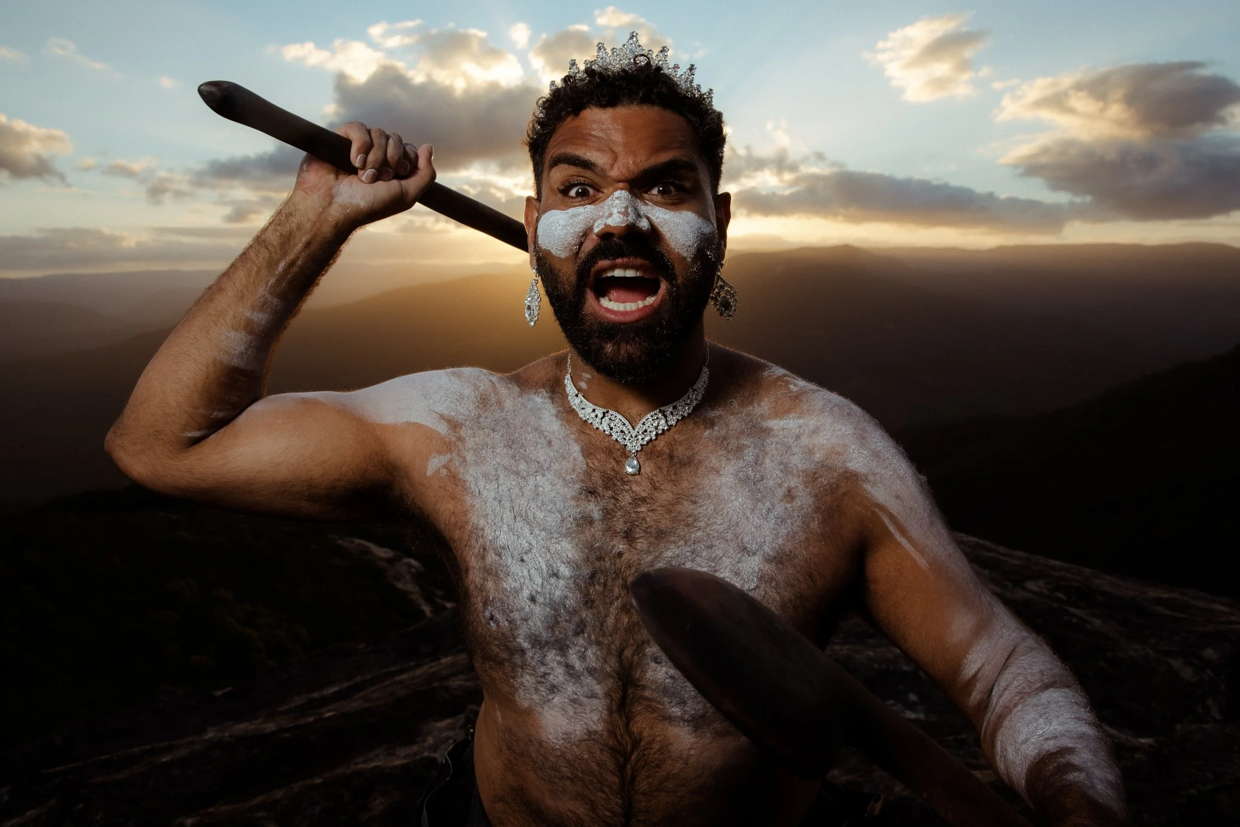 Shaede, painted up, mid-cry with a club raised, the ranges behind at sunset.