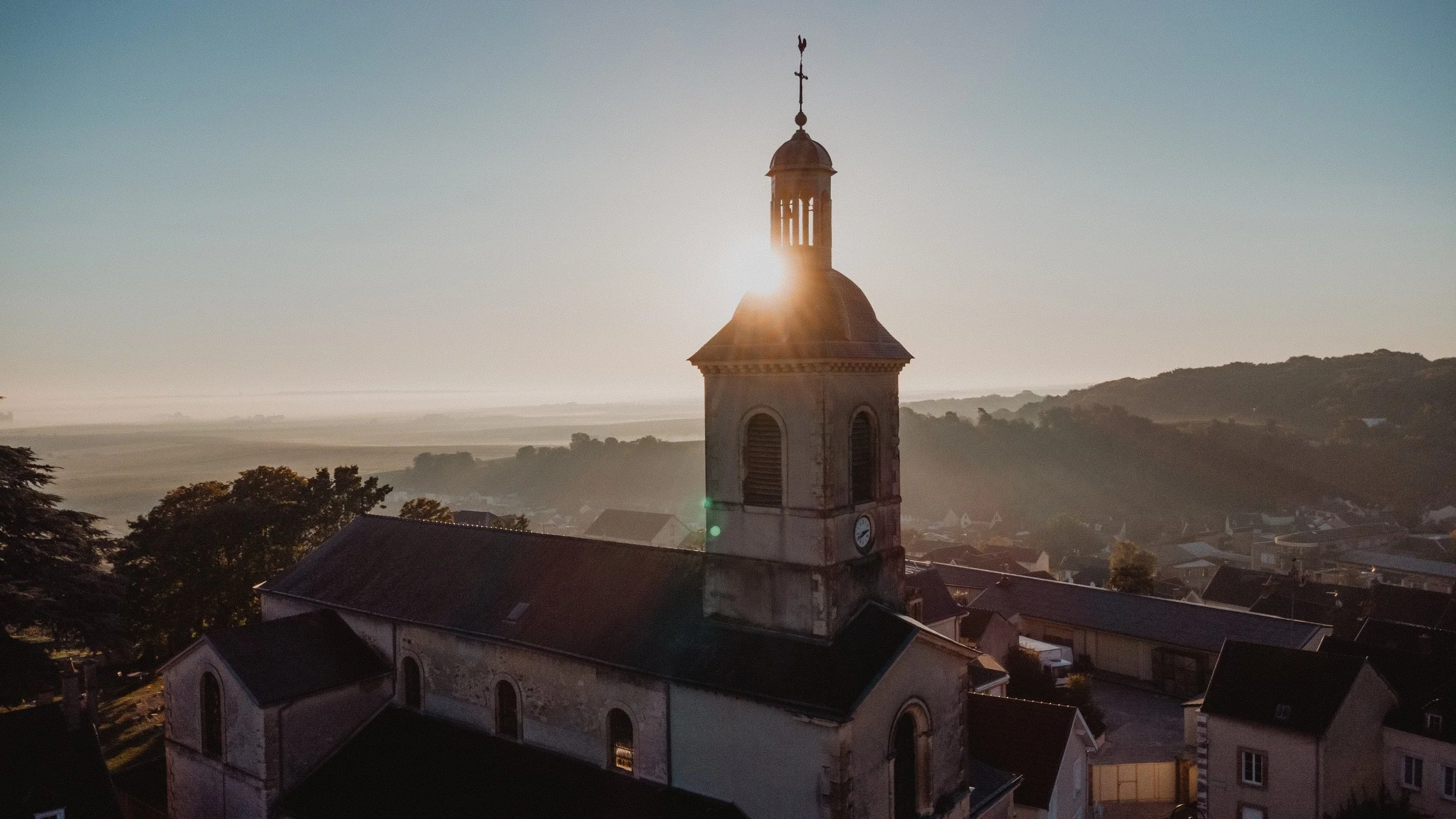 The Verzy bell tower silhouetted against the morning sun, hills behind.