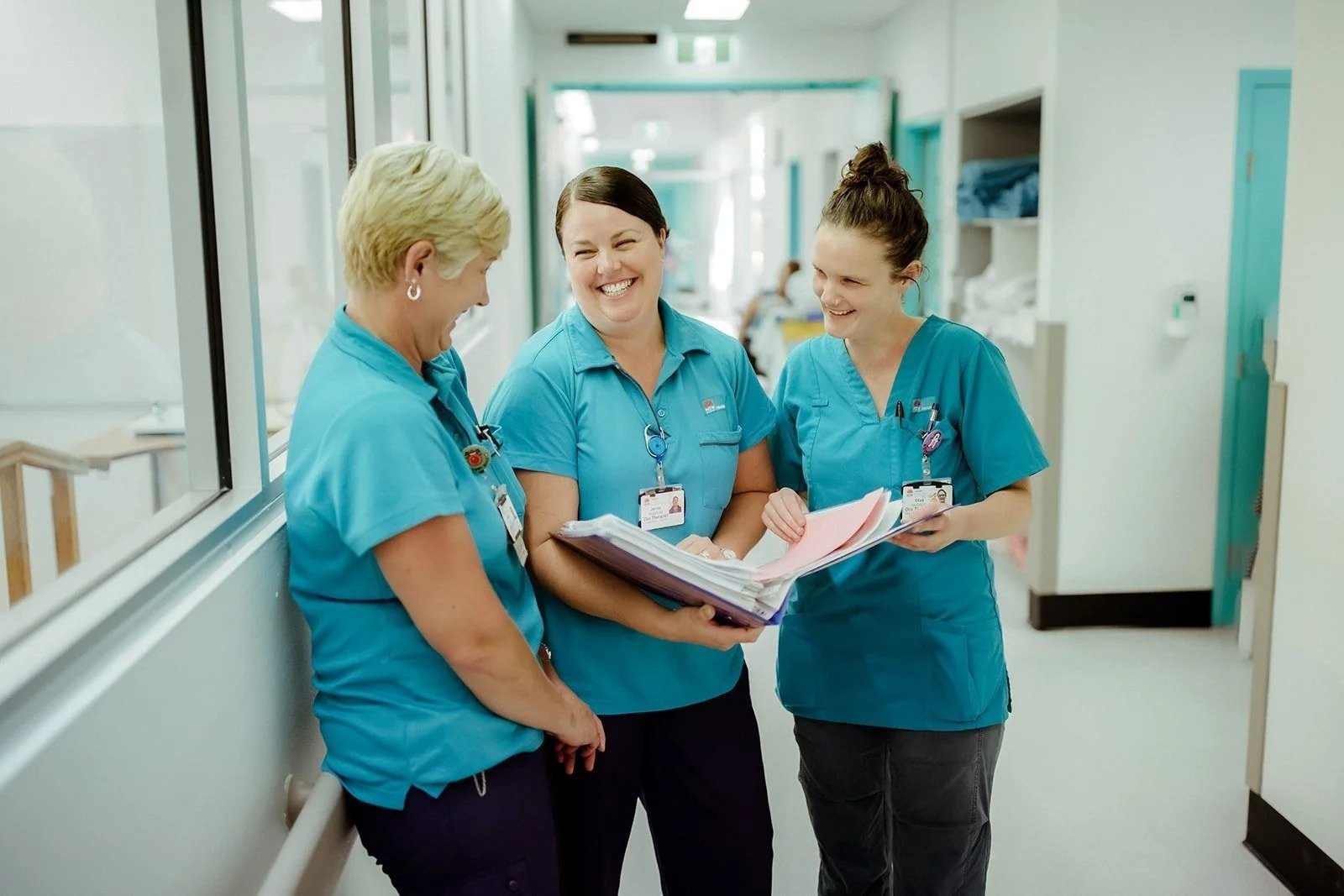 Three nurses in teal scrubs reviewing notes together in a corridor at Wyong Hospital