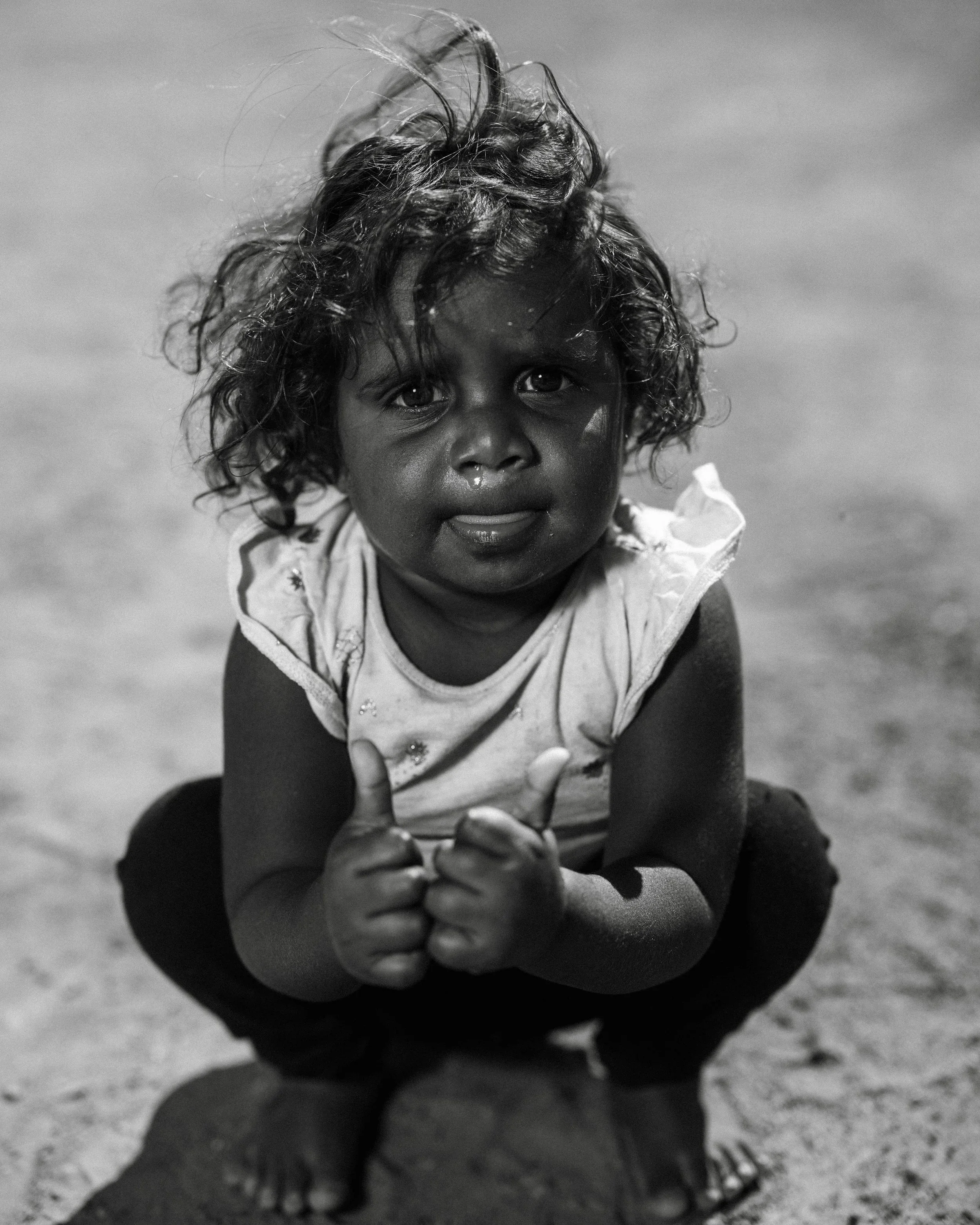 A young child crouching with both thumbs up. Pilbara Portraits, 2025