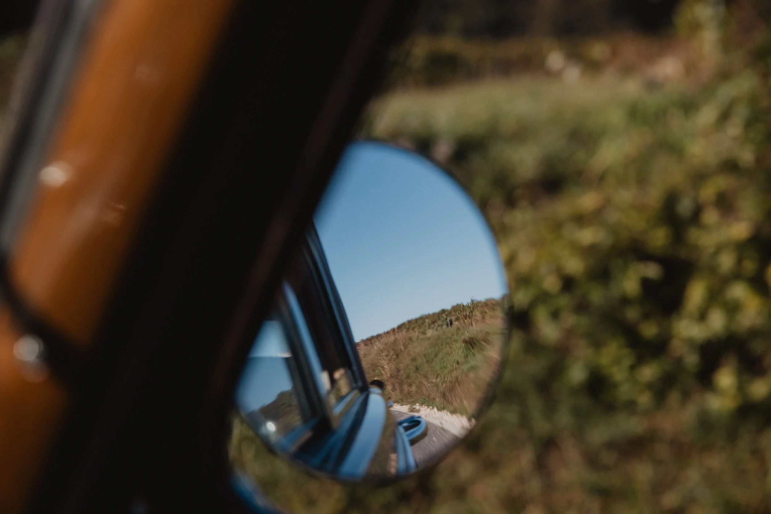 A round wing mirror holds the vineyard hillside inside the dark frame of a vintage car.