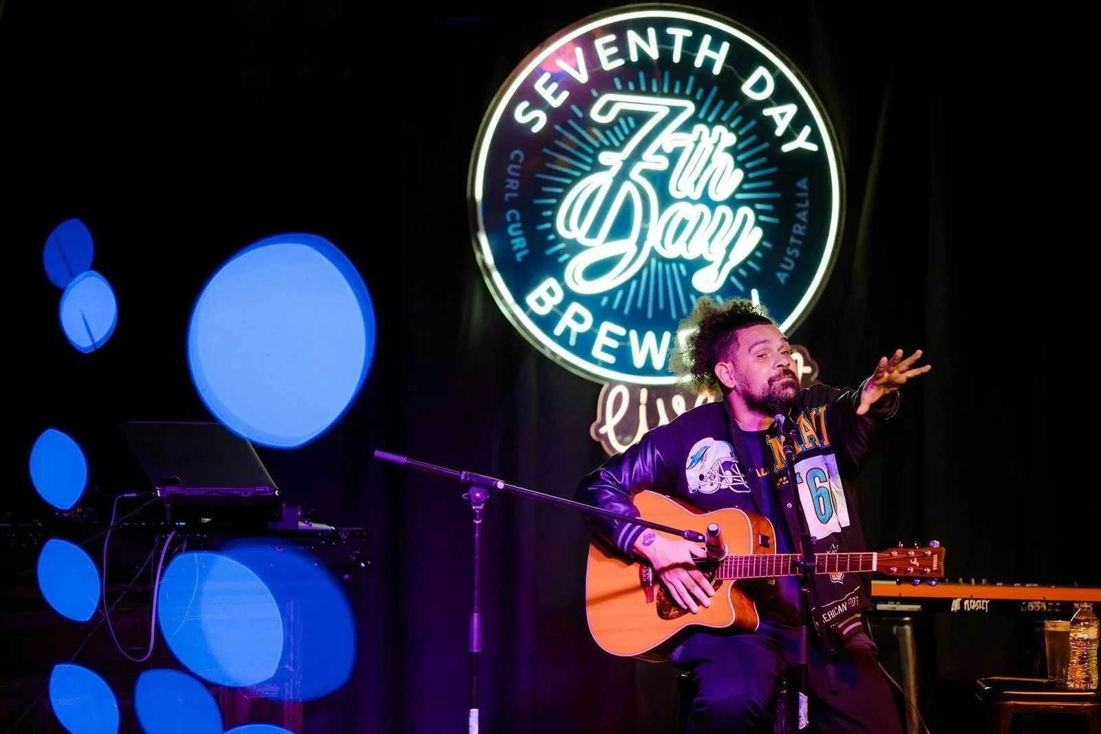 A guitarist performing under the 7th Day Brewery neon sign at Black Winter Block Party, Brookvale