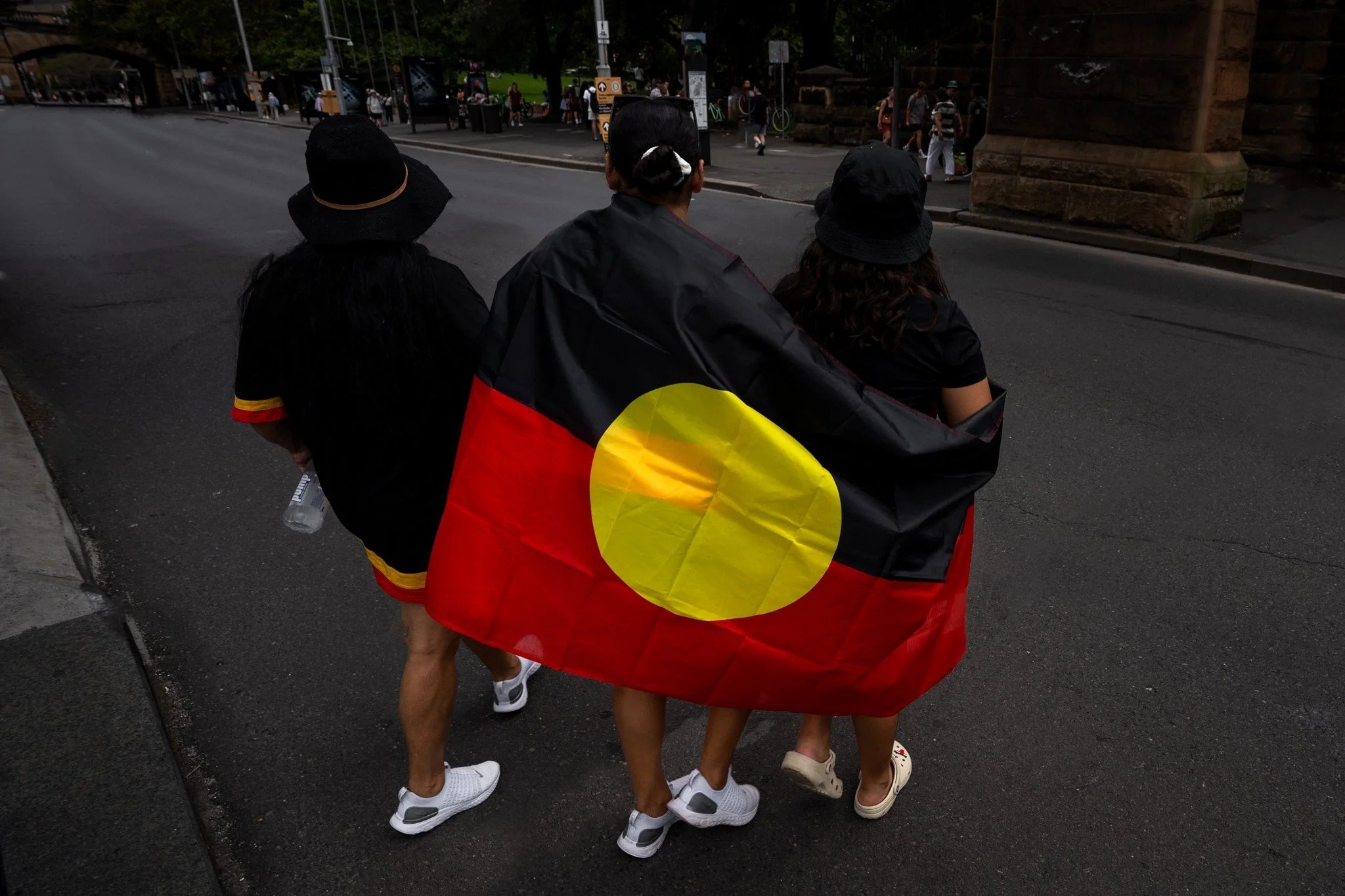 Three people walking with the Aboriginal flag around their shoulders, Invasion Day, Sydney