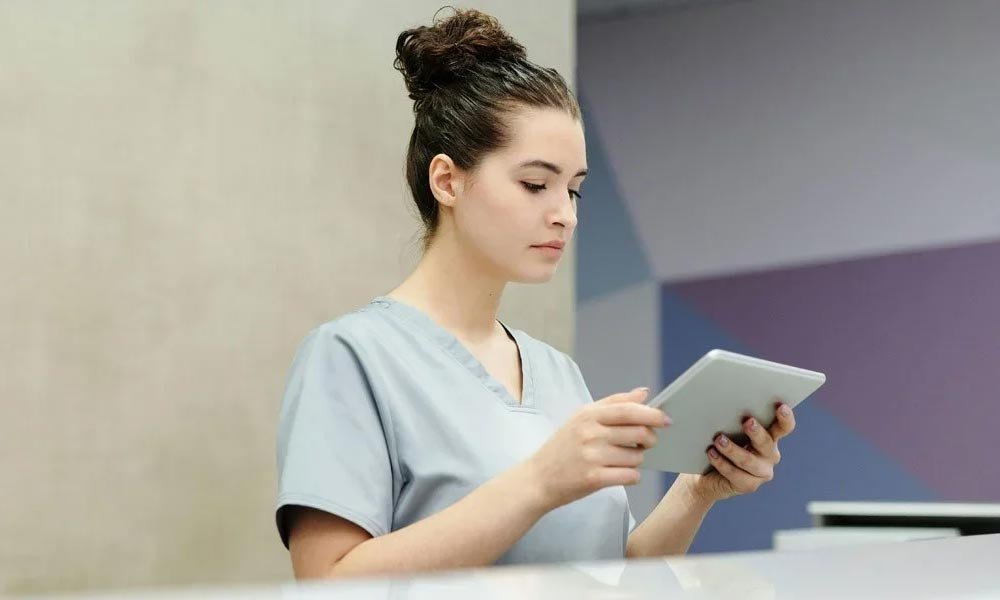 A woman in scrubs is focused on using a tablet. | Feature image for the Fall Risk Assessments page