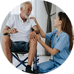Nurse offering support to an older man seated in a wheelchair.